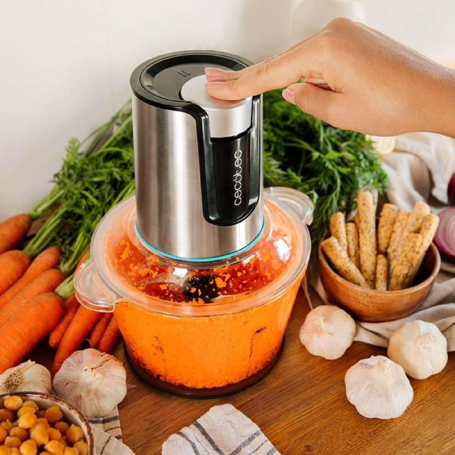 Un robot da cucina con una mano che preme sulla parte superiore, circondato da verdure e ingredienti.