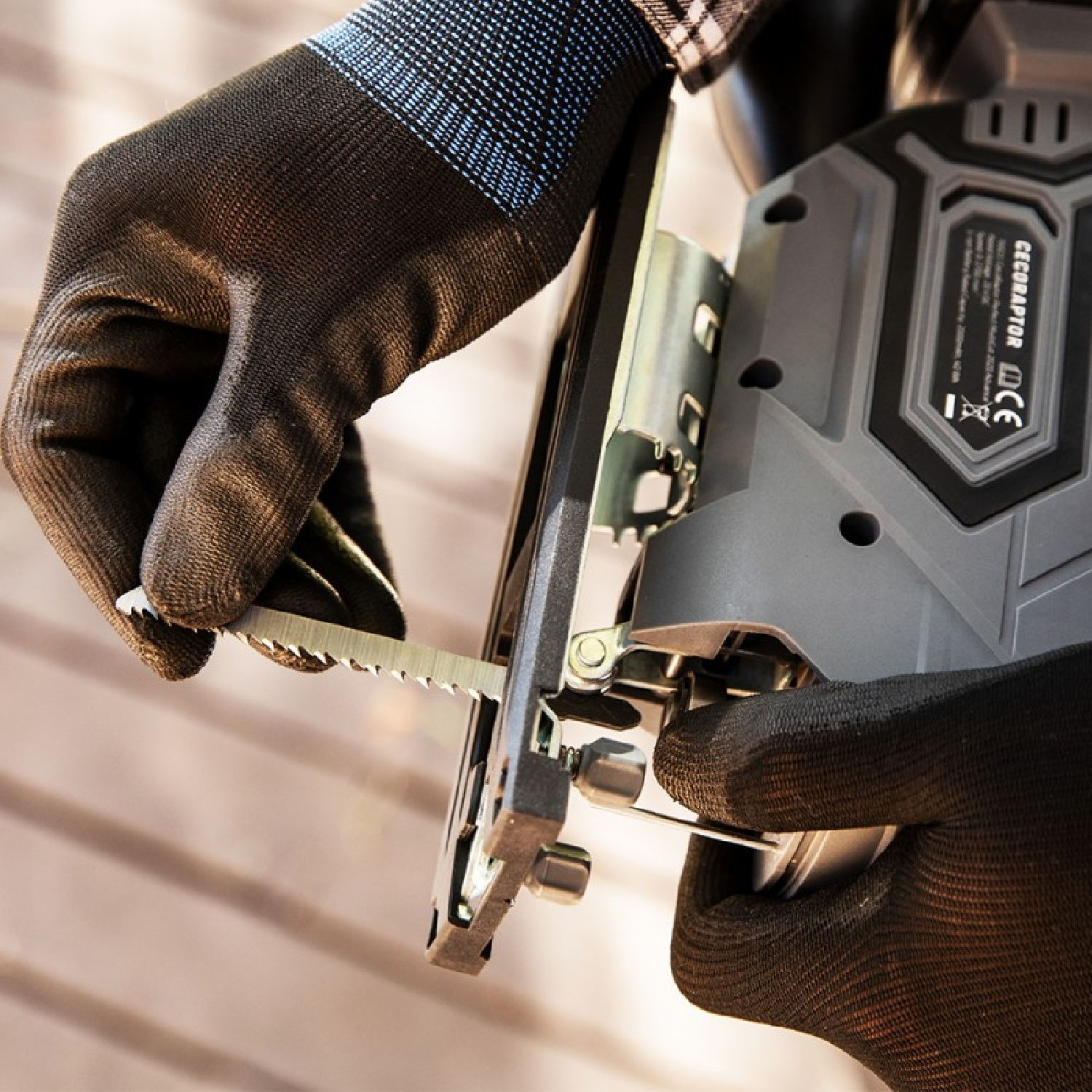 Zbliżenie dłoni osoby używającej wyrzynarki. Mają na sobie czarne rękawice, a piła jest metalowa.