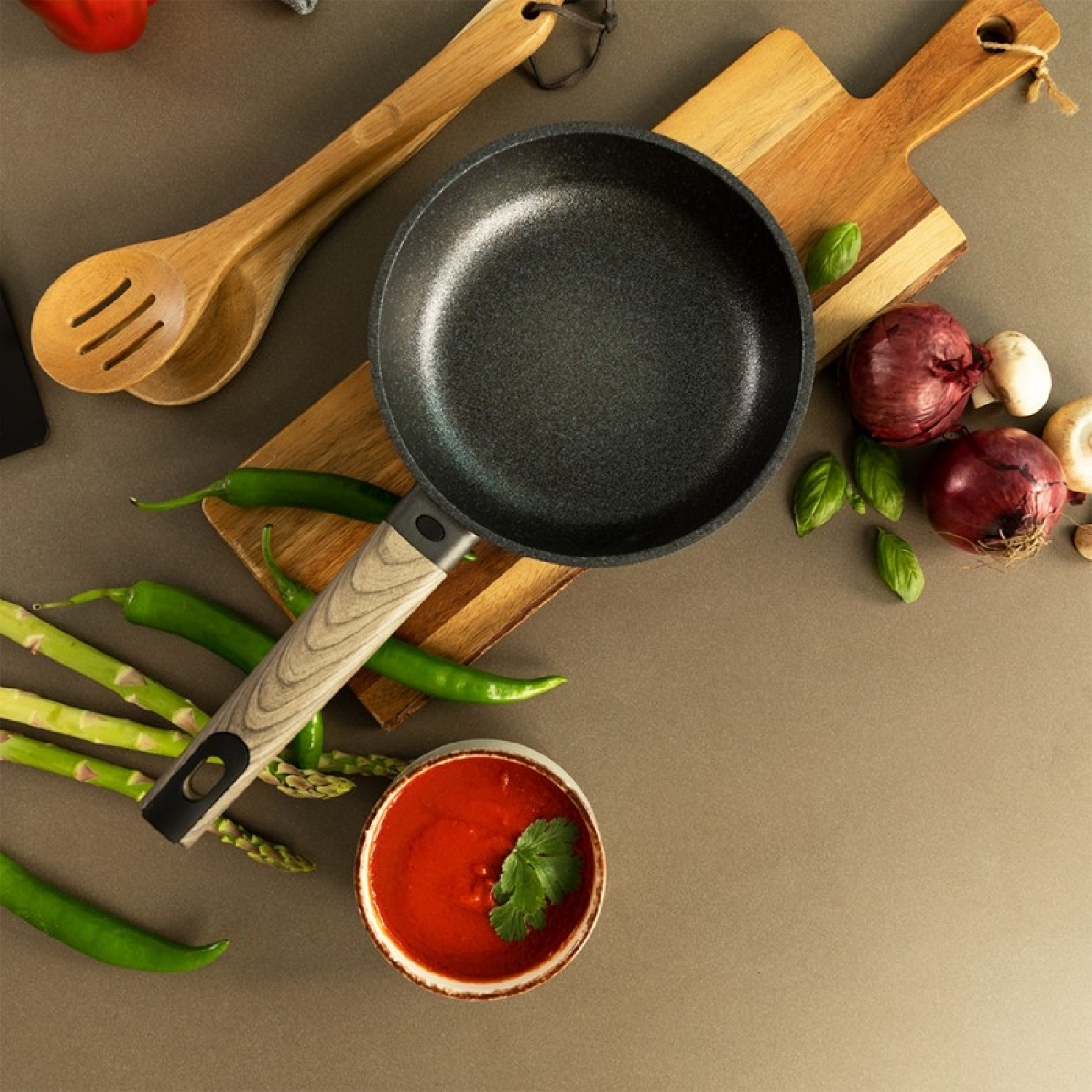 Una padella su un tagliere di legno con verdure e utensili intorno.