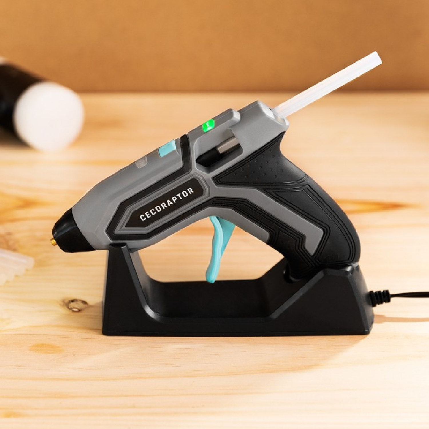 Pistolet do kleju na stojaku. Włożony wkład kleju. Czarno-szary design. Drewniana powierzchnia.