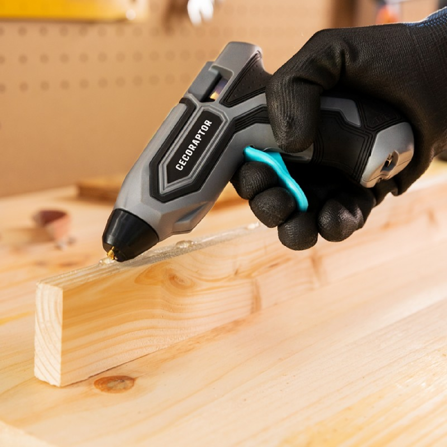 Osoba w czarnej rękawicy używa pistoletu do klejenia deski drewnianej. Tło to warsztat.
