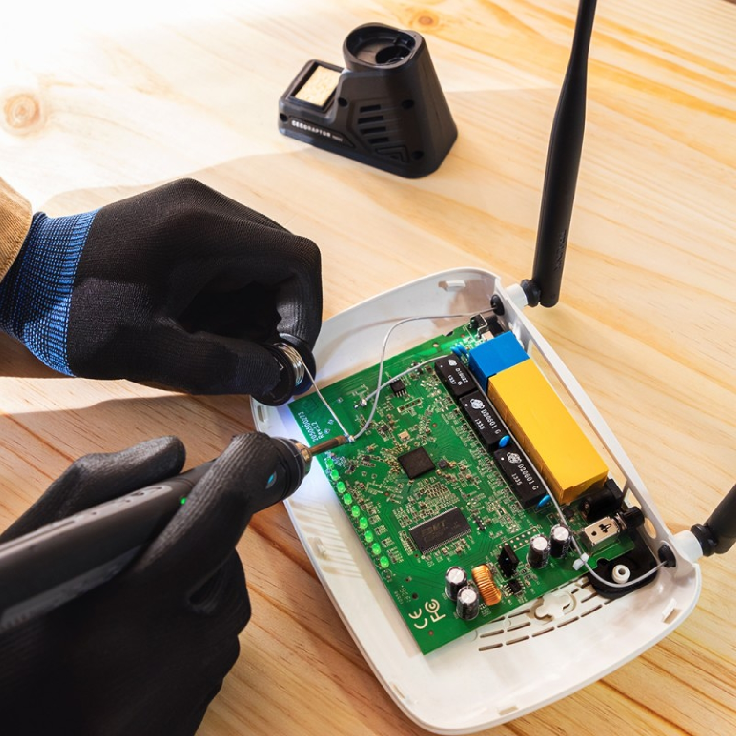 Mani che saldano un circuito stampato. Un saldatore e un router sono su un tavolo di legno.