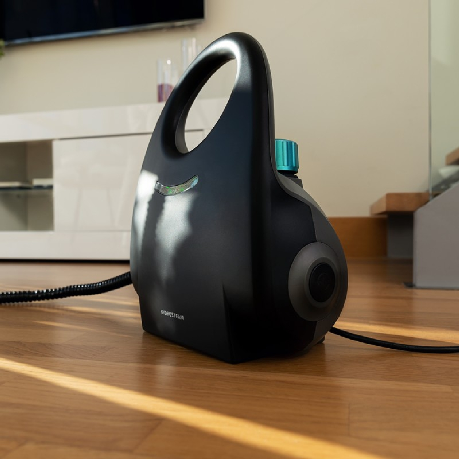 Un pulitore a vapore nero su un pavimento in legno, con una manopola turchese e una maniglia.
