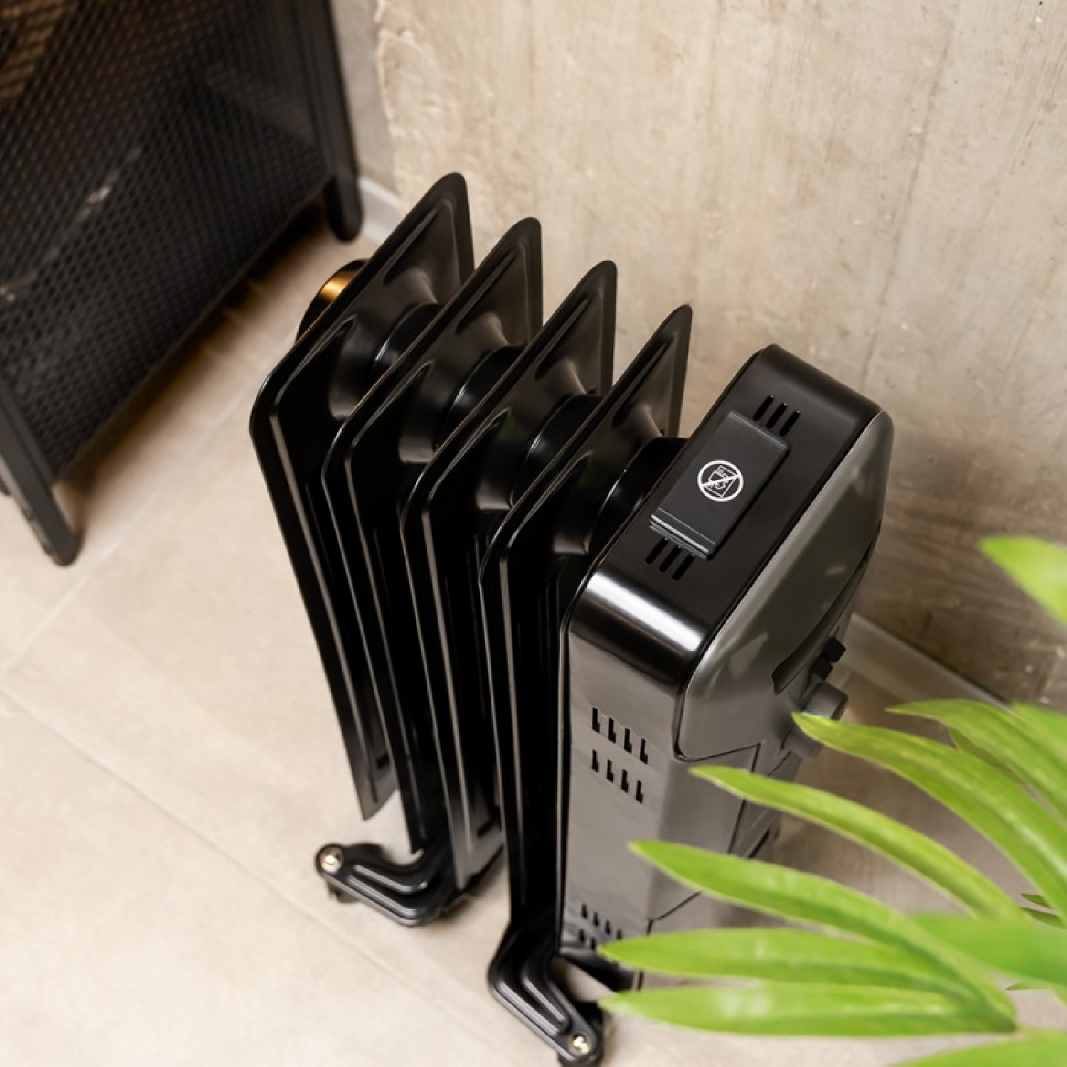 Czarny kaloryfer olejowy jest w pokoju. Zielona roślina jest na pierwszym planie.