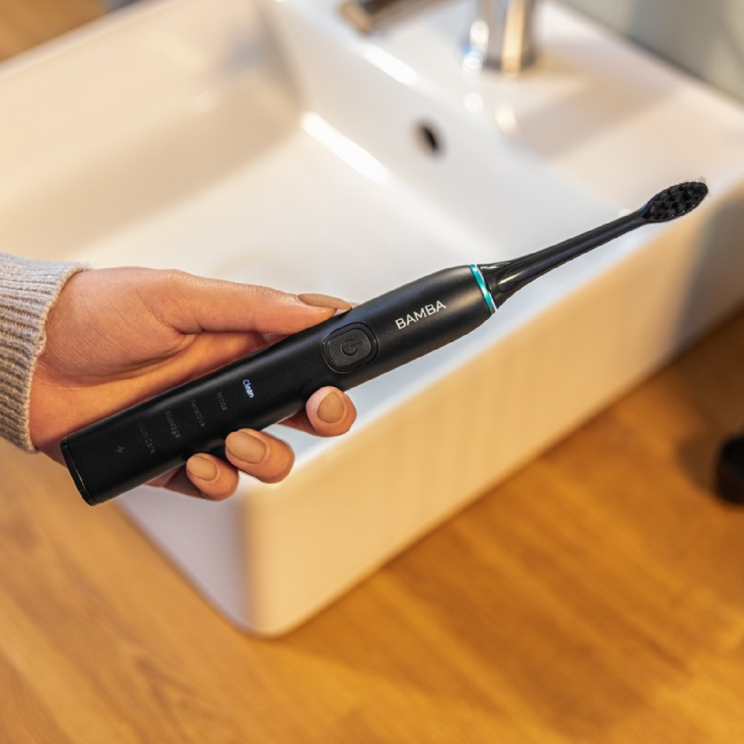 Spazzolino elettrico nero in mano, con testo e lavandino.