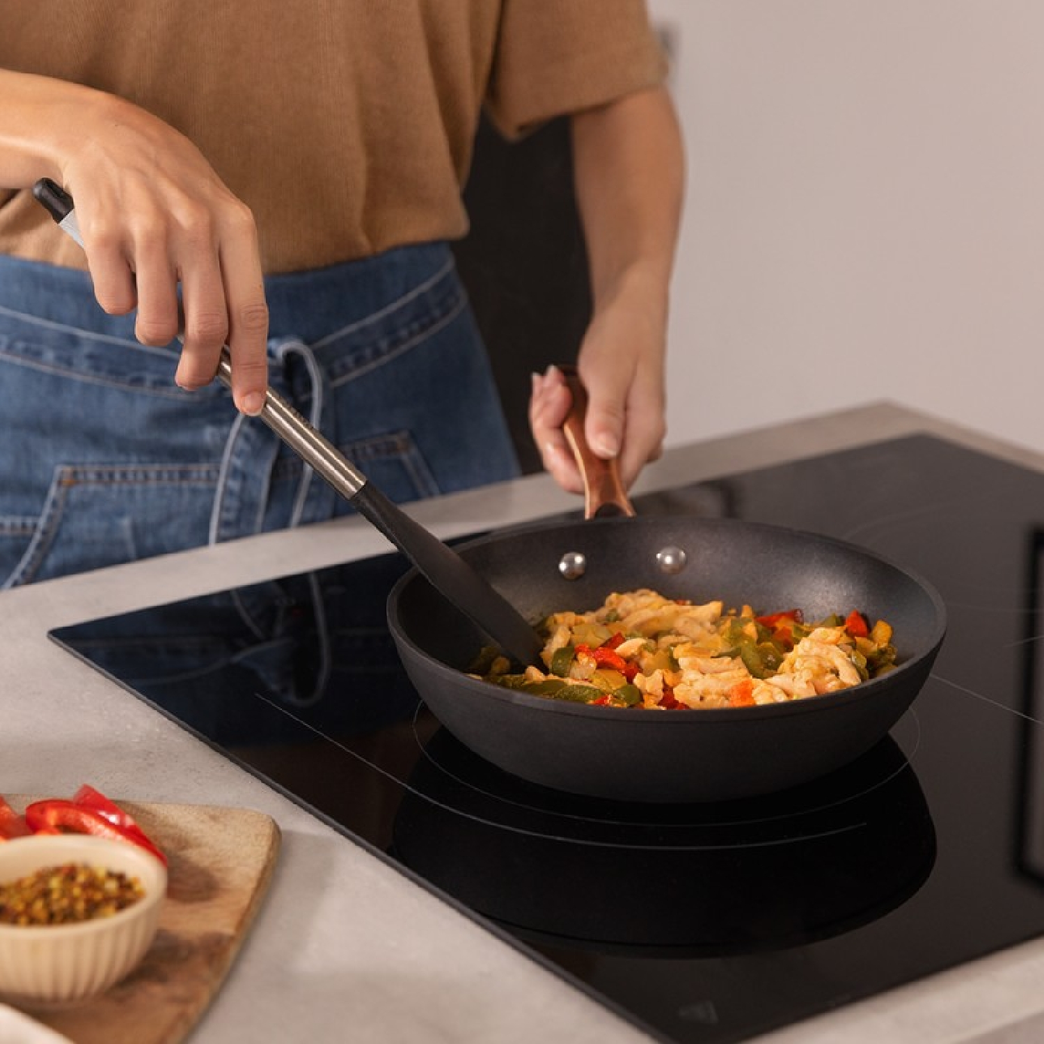 Ręce gotujące kurczaka i warzywa na patelni na płycie grzejnej.