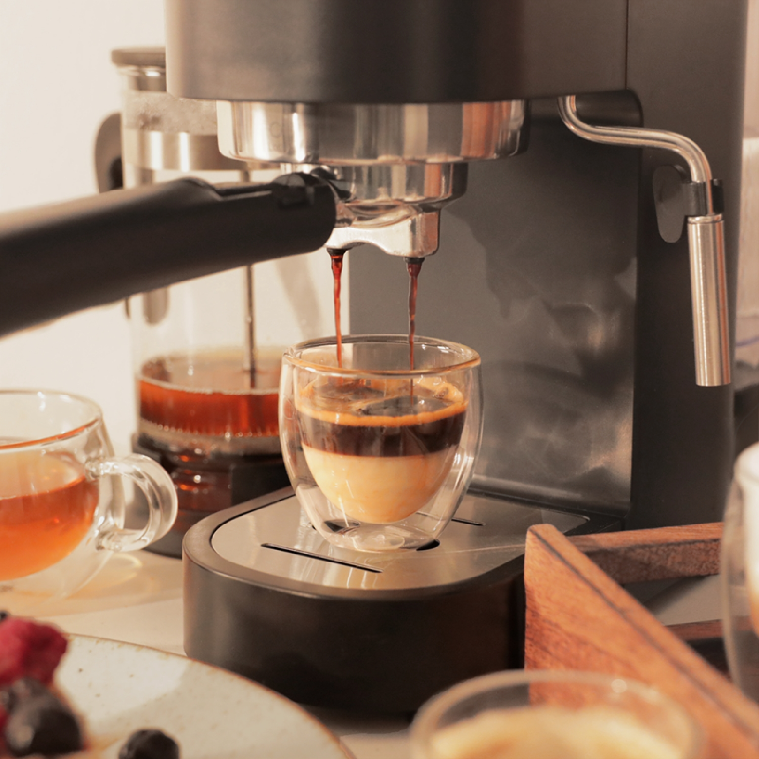 Espressomaschine gießt Kaffee in eine Glastasse. Andere Kaffee- und Teeartikel sichtbar.