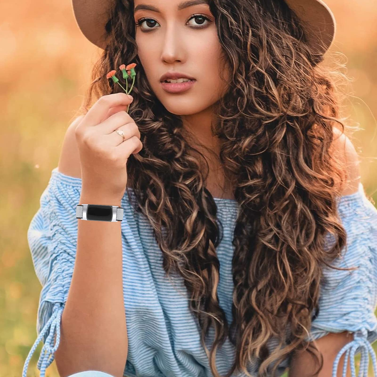 Mujer con cabello rizado usando una pulsera, sosteniendo una flor en un entorno borroso al aire libre.