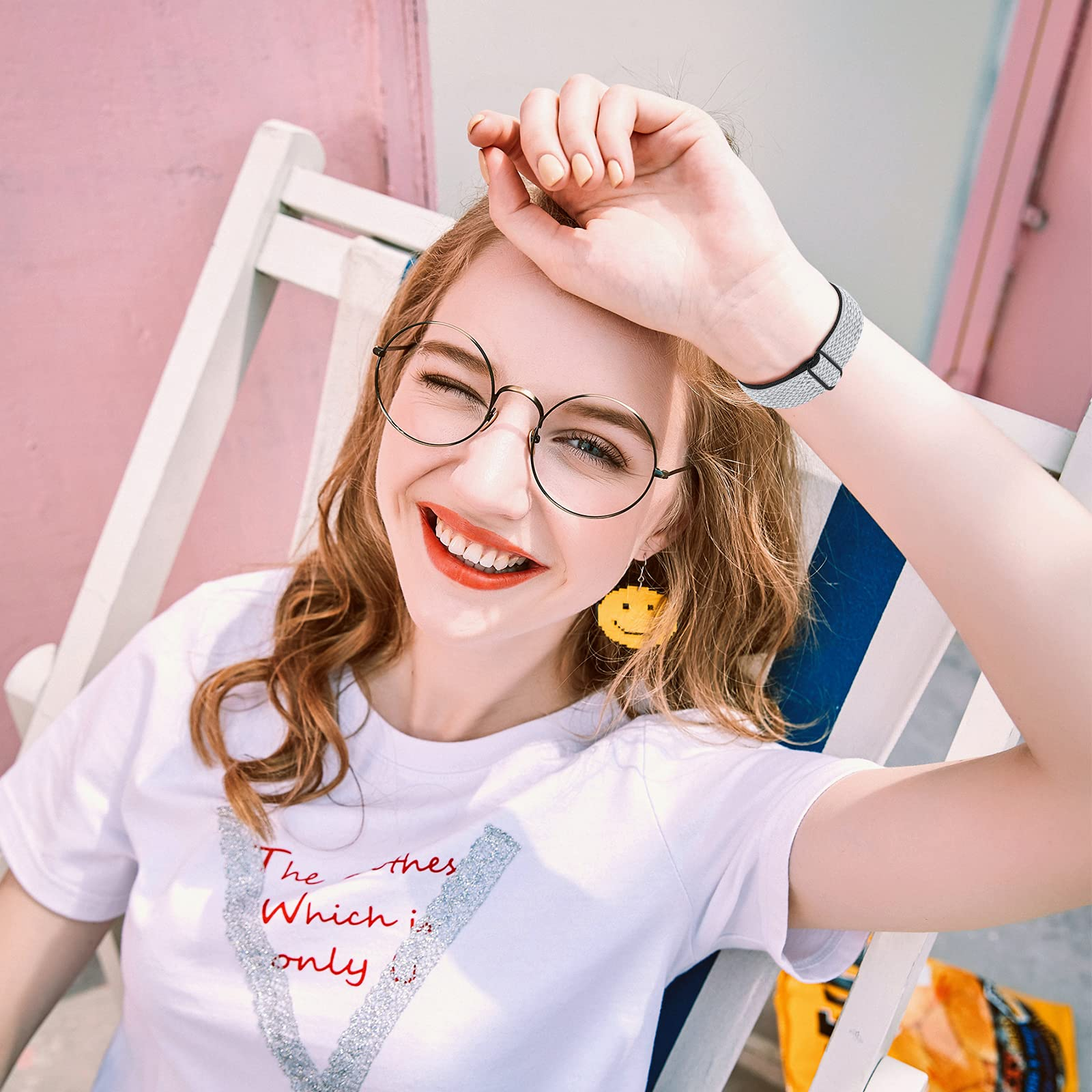 Una mujer sonriente con gafas redondas y una pulsera. Lleva una camisa blanca y pendientes amarillos.