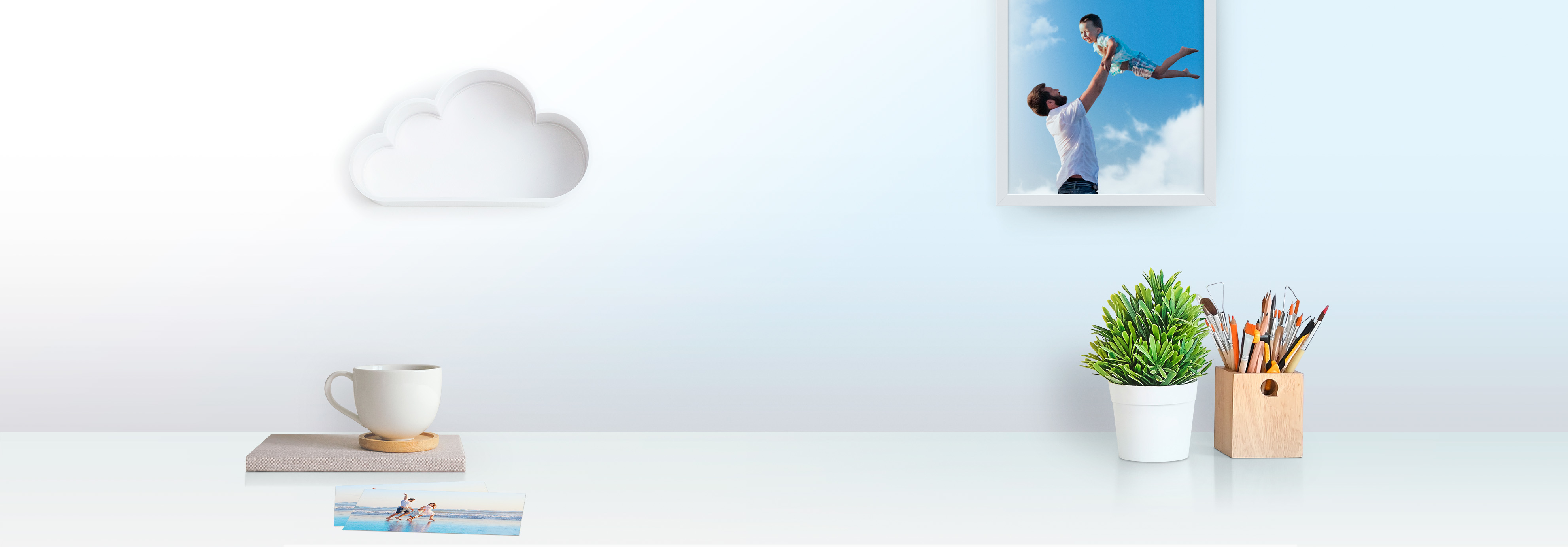 Białe biurko z dekoracją w kształcie chmury, zdjęciem ojca i dziecka, rośliną i filiżanką kawy.