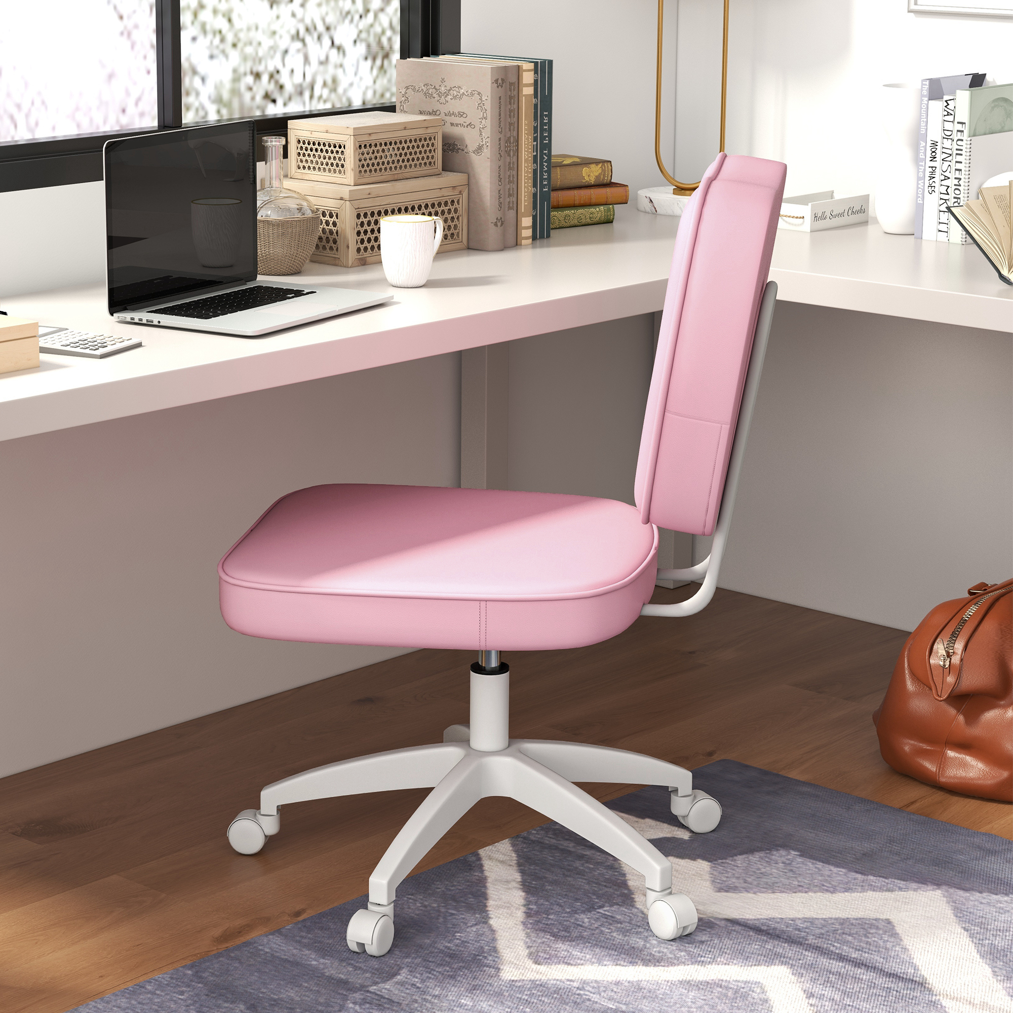 Una silla de oficina rosa está en un escritorio blanco. Hay libros y un portátil.