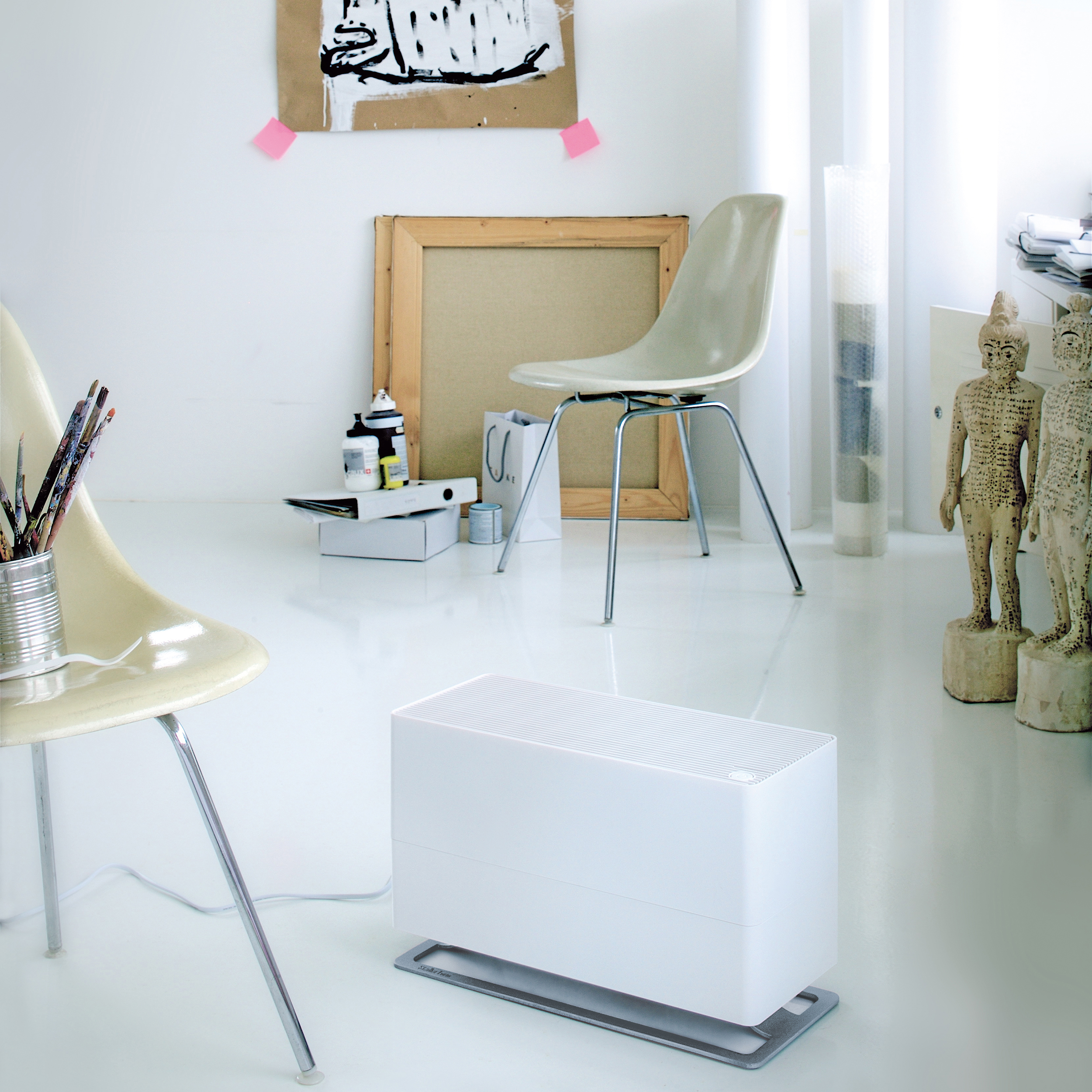 Ein weißes Zimmer mit einem weißen Luftreiniger. Es gibt zwei Stühle, Kunstwerke und Statuen.