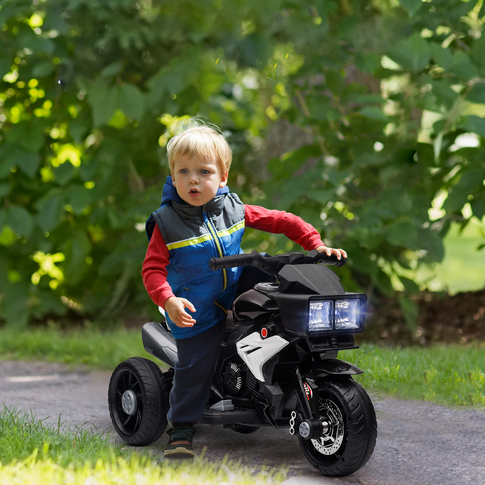 Un niño pequeño montando una moto de juguete negra y roja en un camino de hierba.