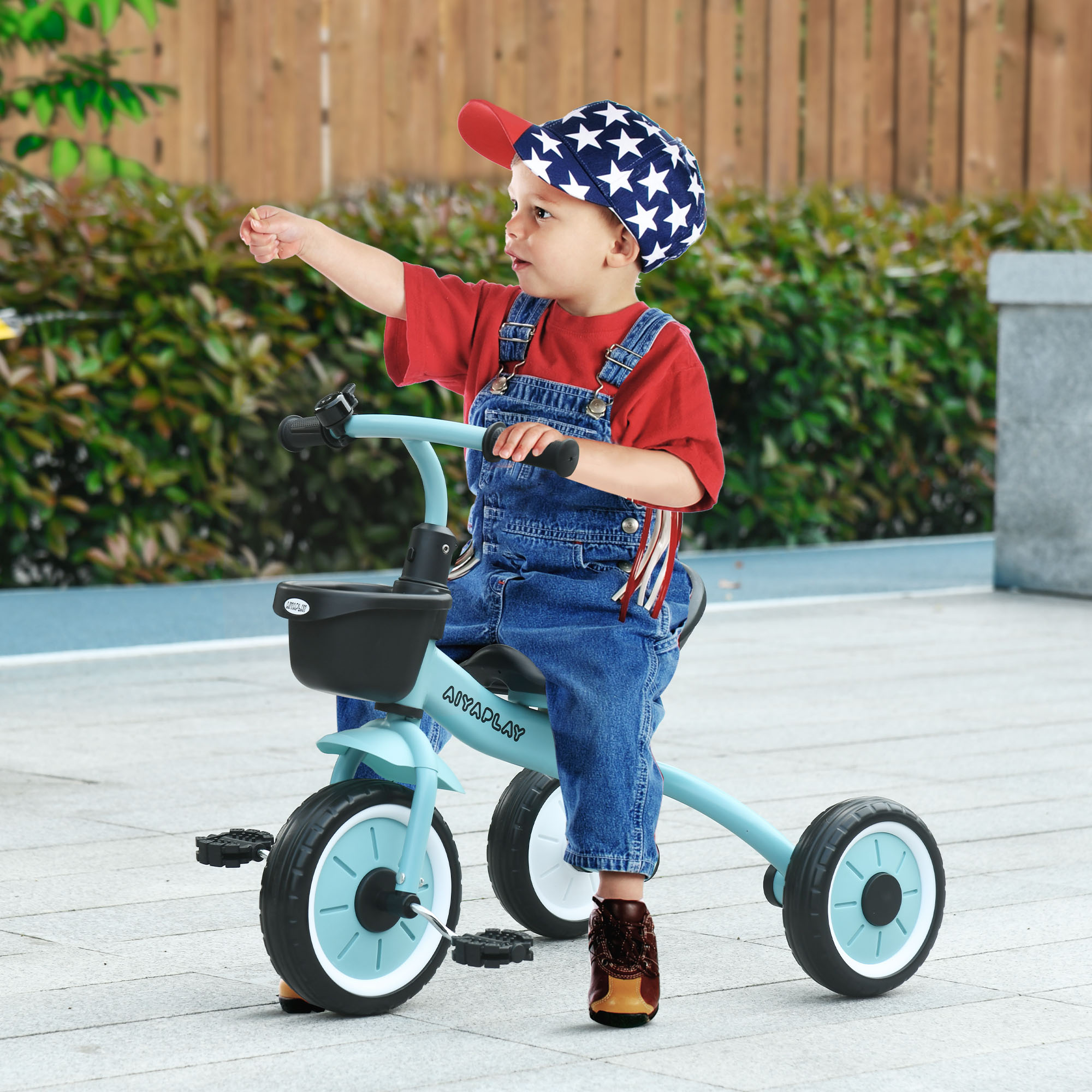 Un bambino piccolo che va in triciclo blu, indicando verso l'alto. Il bambino indossa un cappello e una tuta.