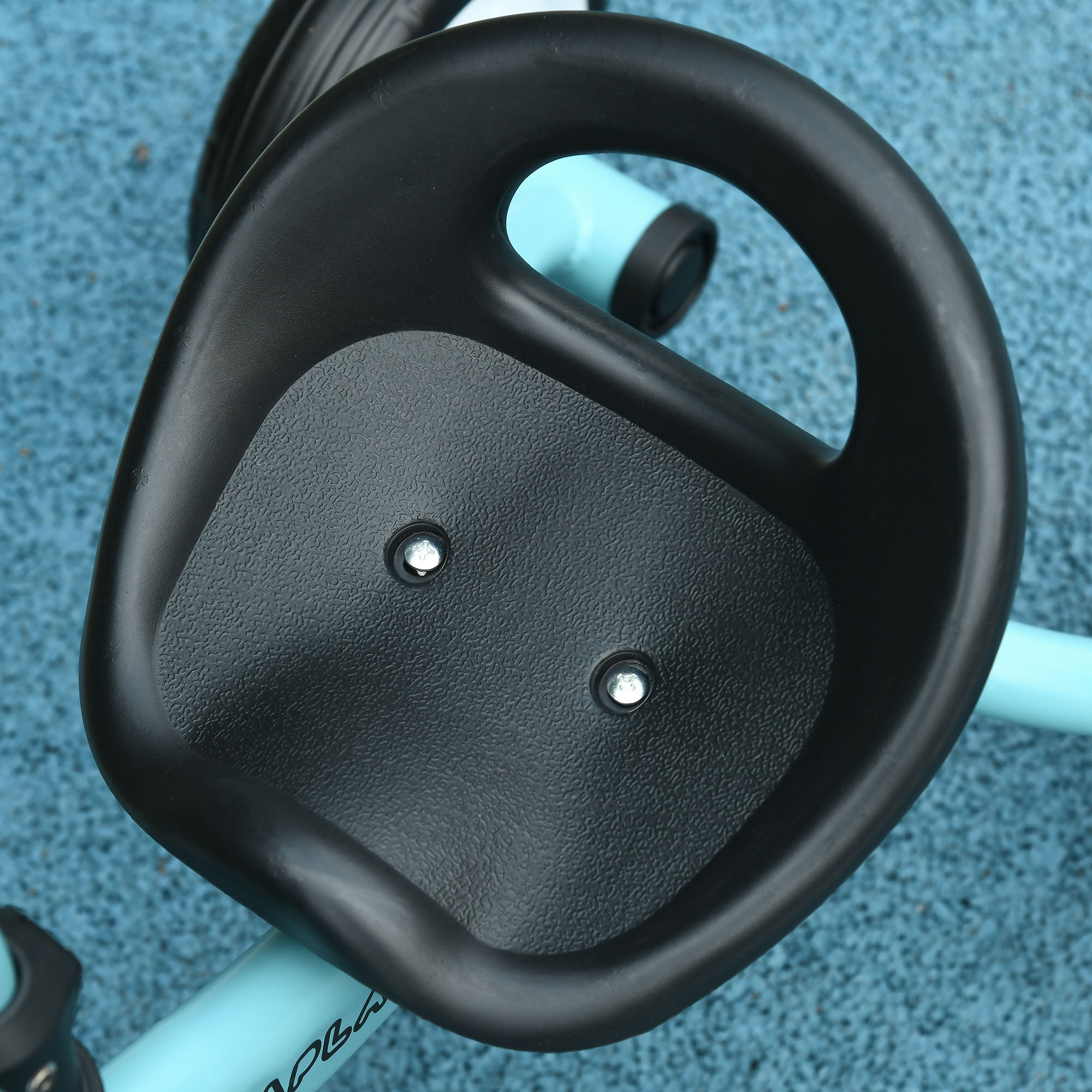 Primer plano del asiento negro de un triciclo infantil. Fondo de superficie azul.