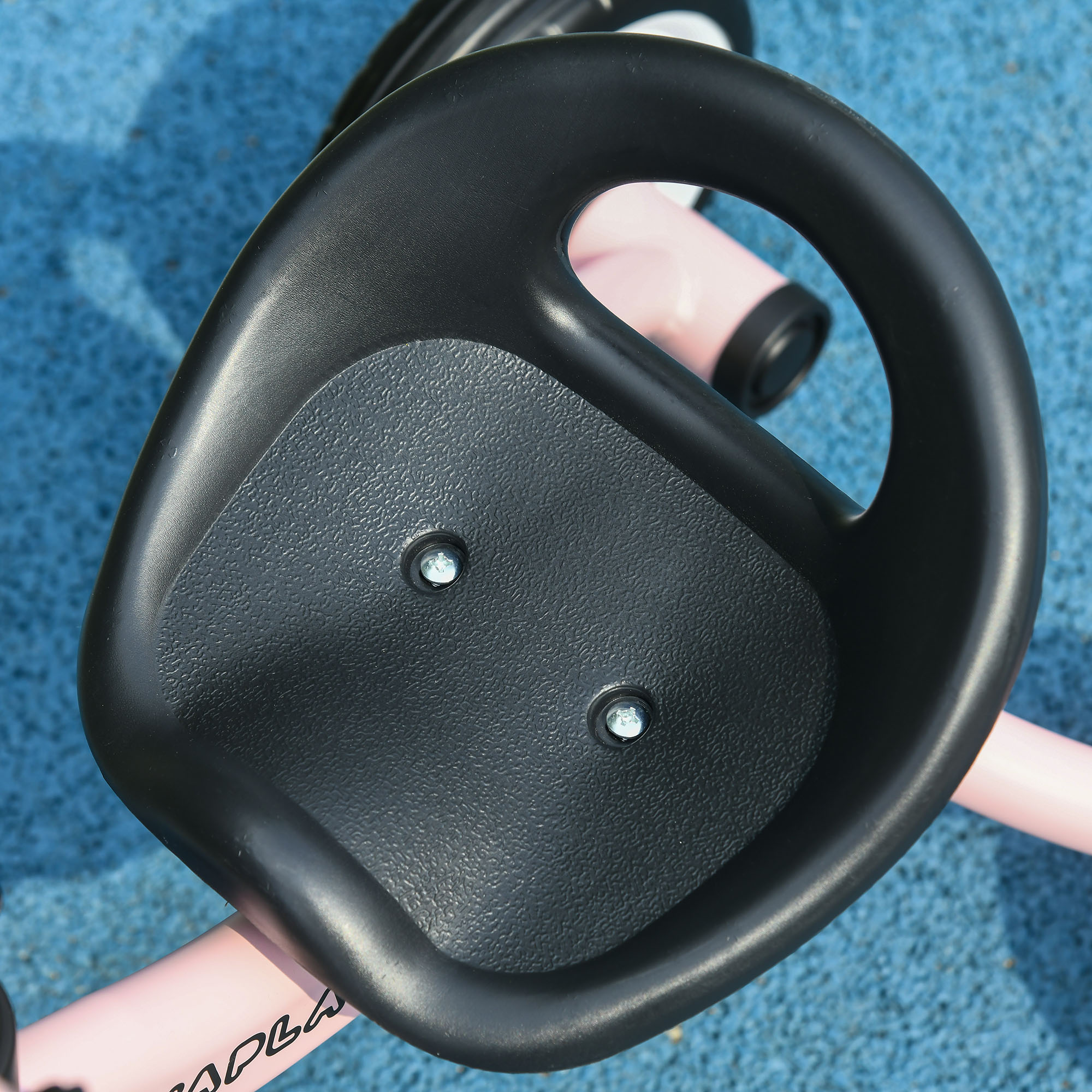 Primer plano del asiento de un triciclo de plástico negro con dos pernos, sobre una superficie azul.