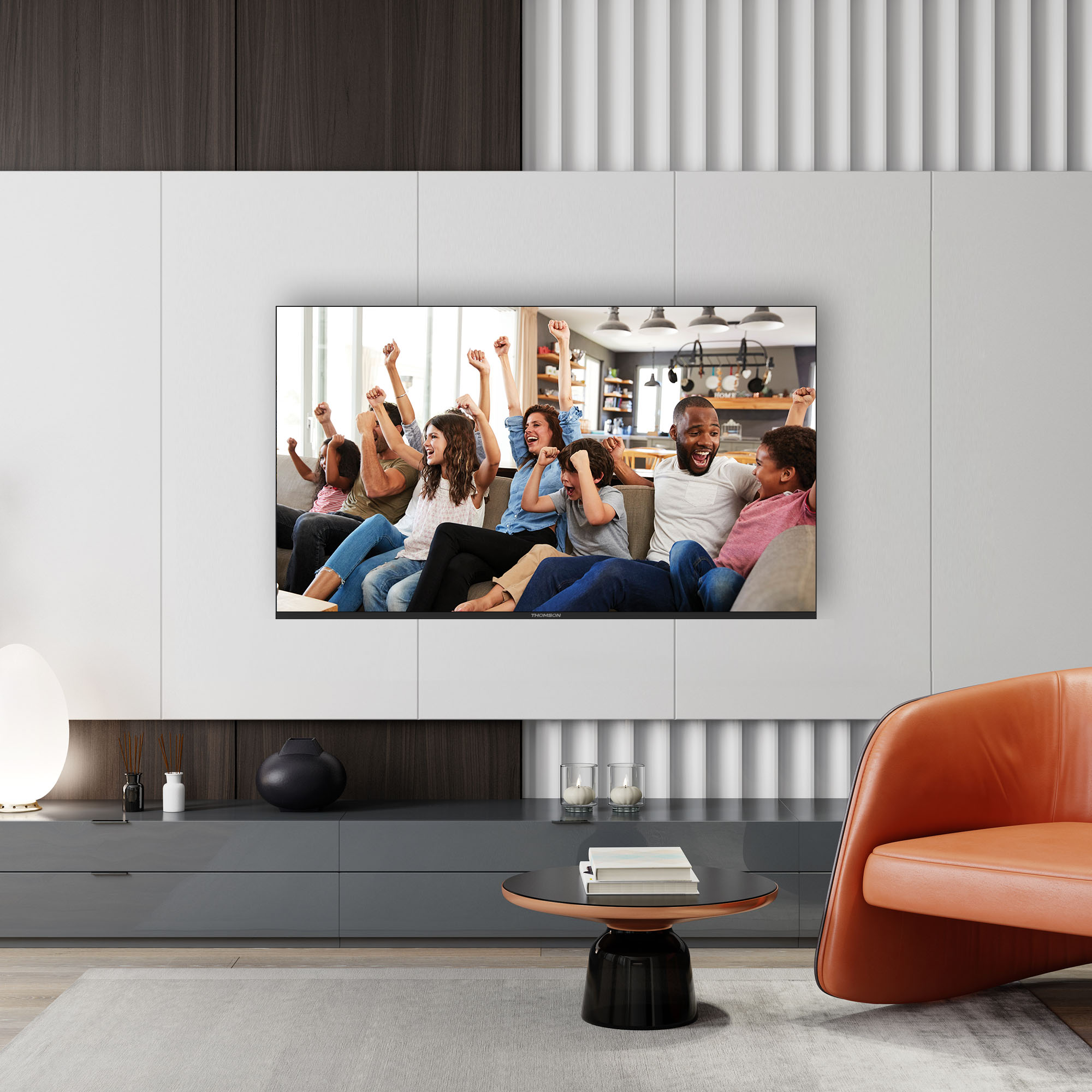 Sala de estar con TV mostrando a una familia celebrando. Pared blanca, armarios grises, silla naranja.