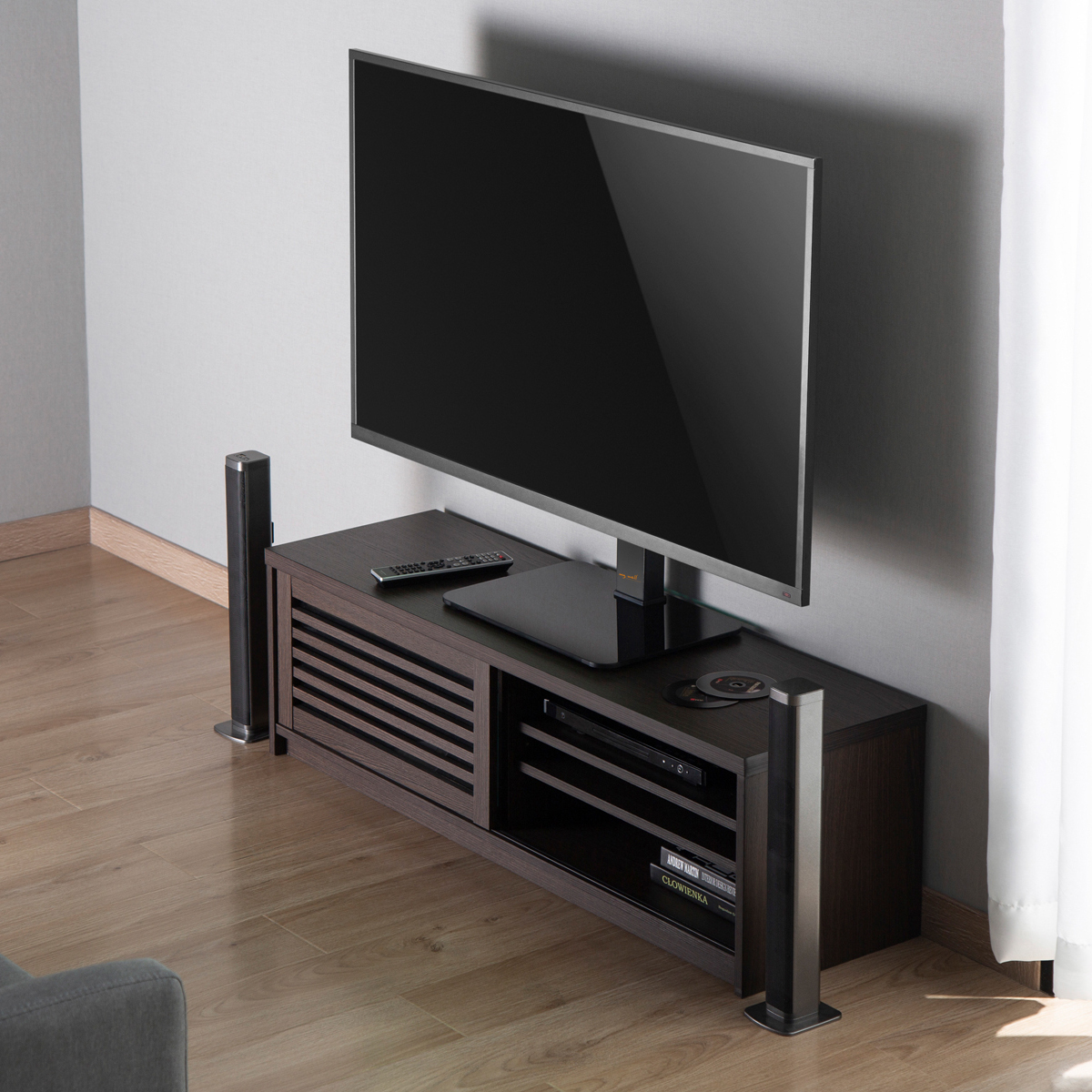 Fernseher auf einem dunklen Holzschrank mit Lautsprechern auf jeder Seite. Holzboden, graue Wand.