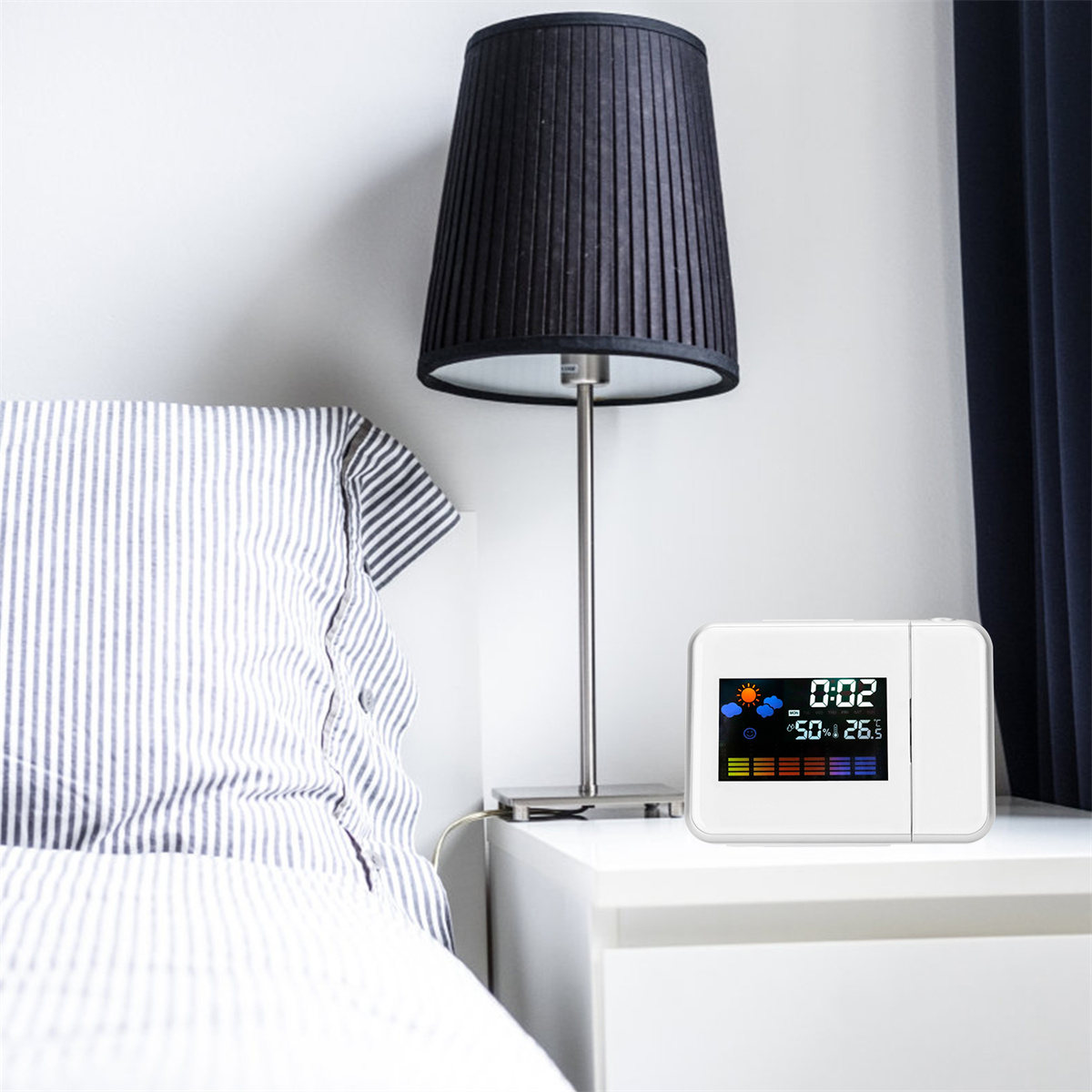 Digitaluhr auf Nachttisch neben Lampe und Bett.