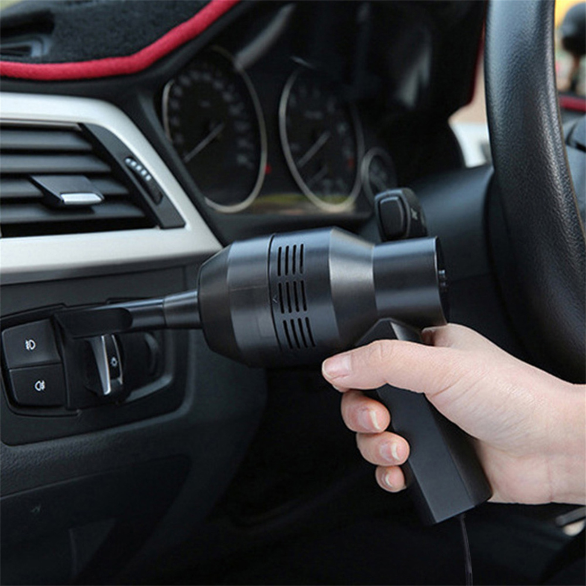 Eine Hand, die einen schwarzen Staubsauger für Autos im Inneren eines Autos in der Nähe von Lüftungen hält.