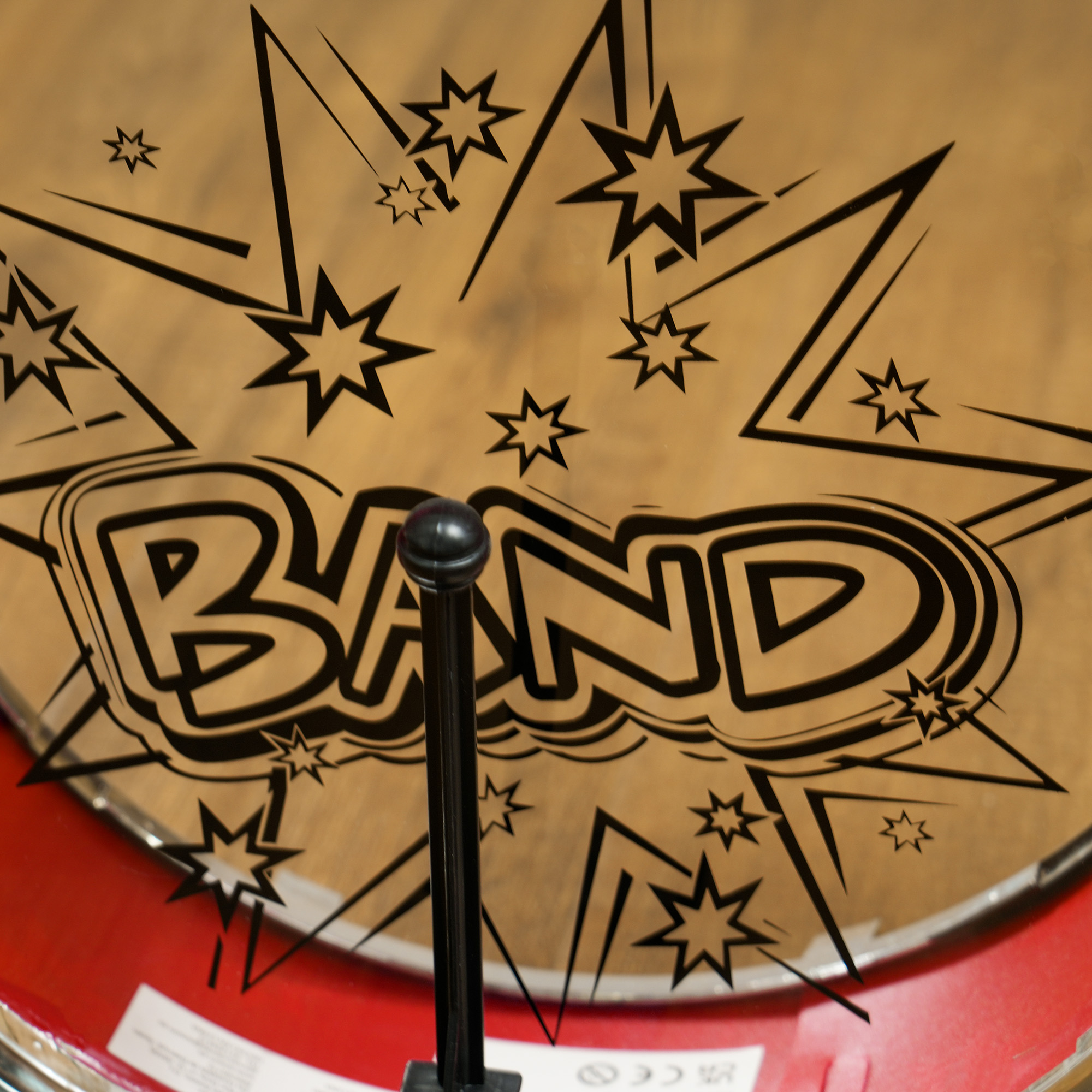 Un parche de tambor con la palabra 'BAND' y diseños de estrellas. Una baqueta negra es visible.