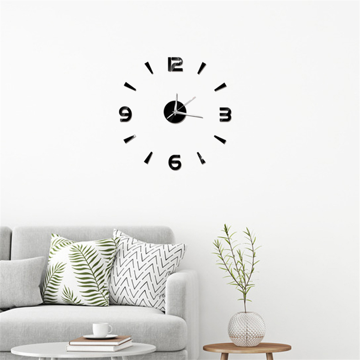 Eine Wanduhr mit schwarzen Zahlen und Zeigern. Sofa und Kissen davor. Pflanze und Tisch.