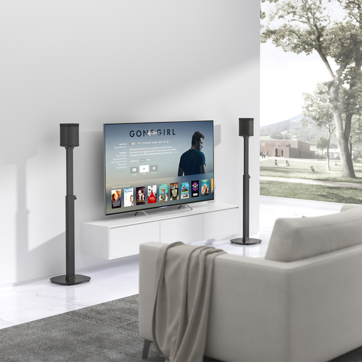 Fernsehbildschirm mit Filminformationen, flankiert von zwei Lautsprechern. Ein weißes Sofa davor, Baum draußen.