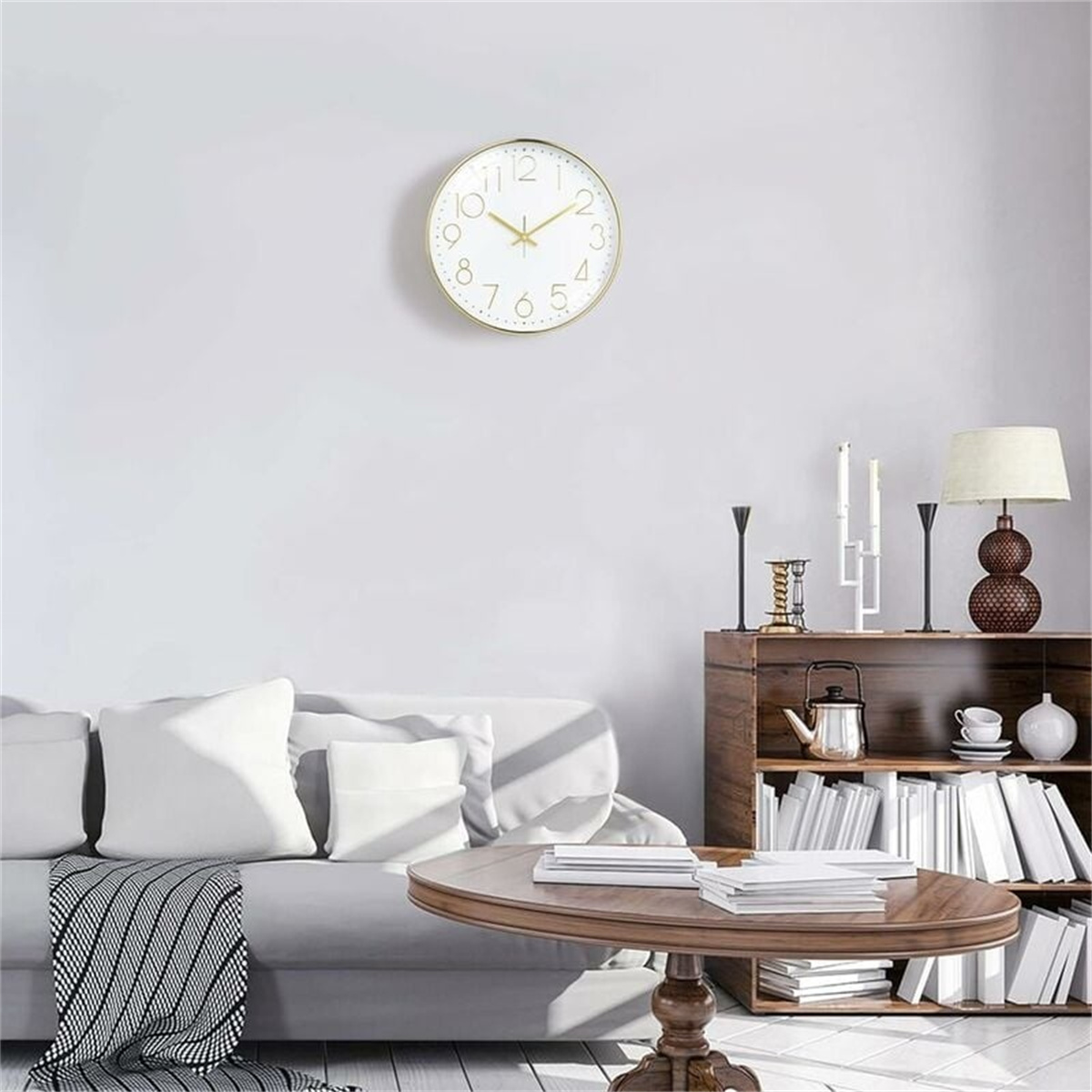 Eine goldgerahmte Uhr an einer weißen Wand. Ein Bücherregal aus Holz mit Büchern und ein Sofa.