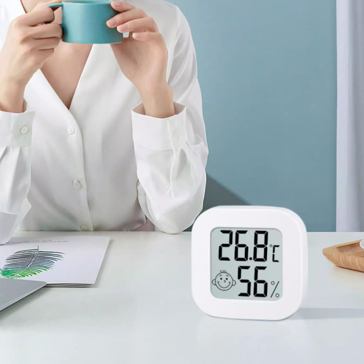 Frau in Weiß hält einen türkisfarbenen Becher, Thermometer zeigt 26,8°C und 56%.