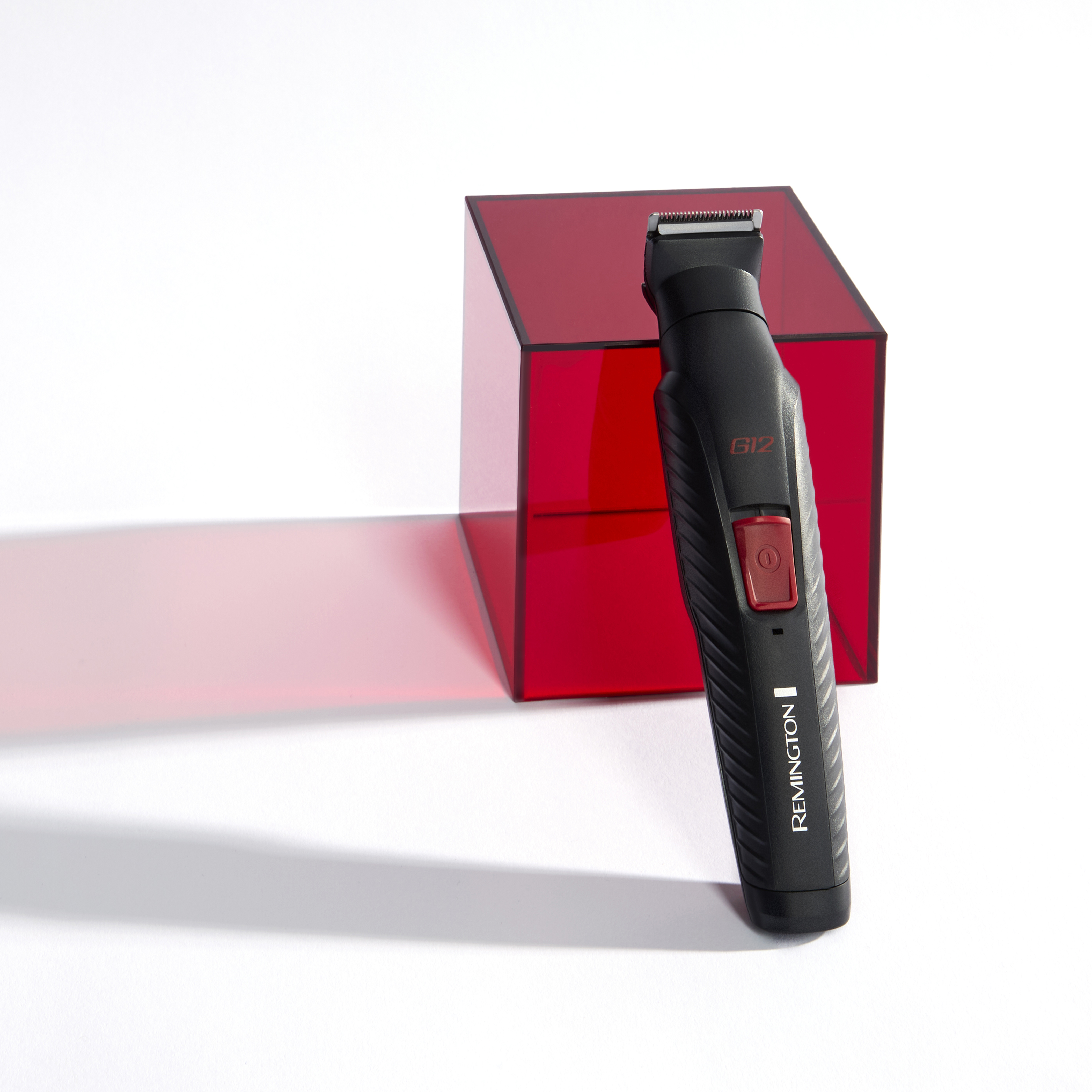Rasoio elettrico nero con un oggetto rosso a forma di cubo su una superficie bianca.