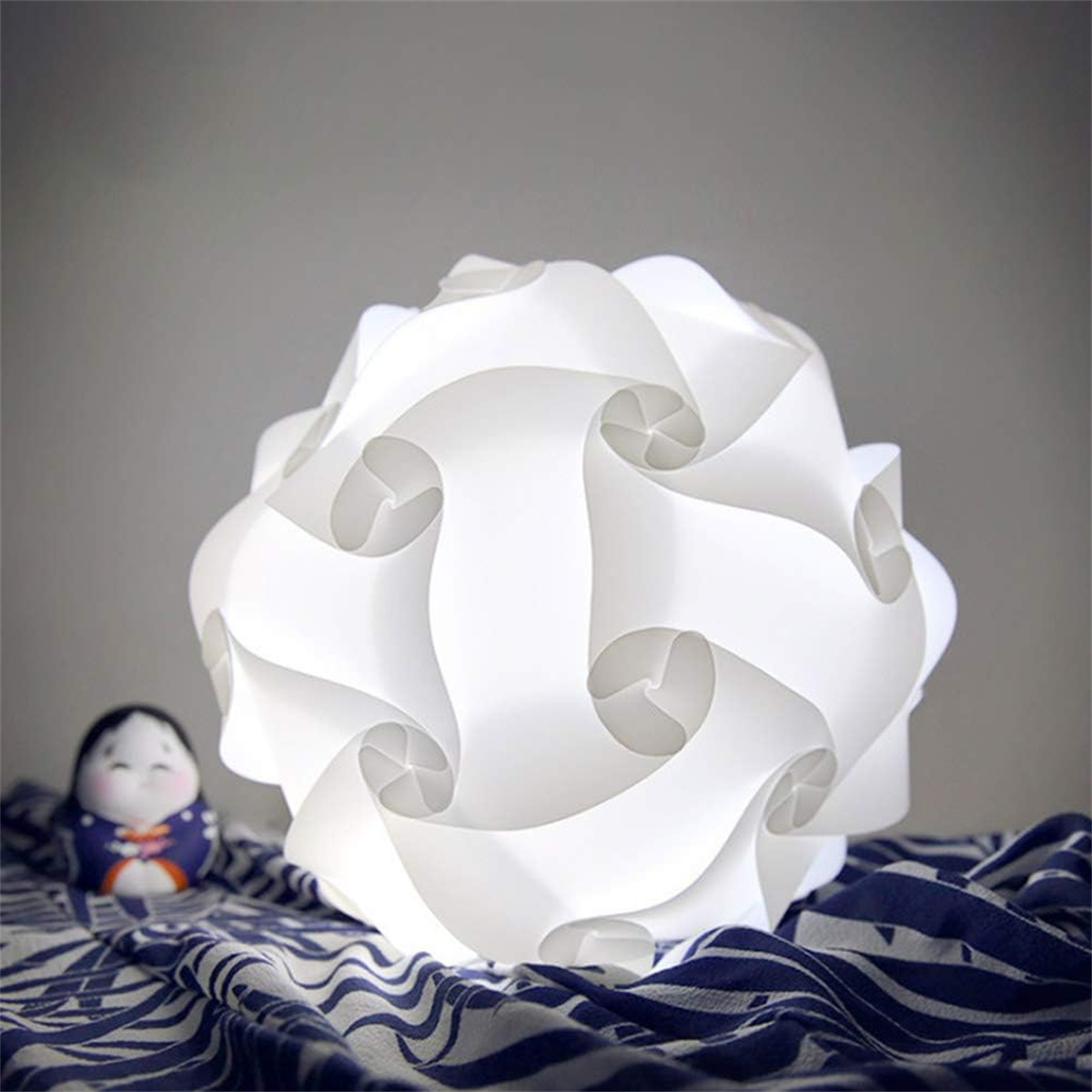 Weiße geometrische Lampe auf blau gemustertem Stoff mit Puppe.
