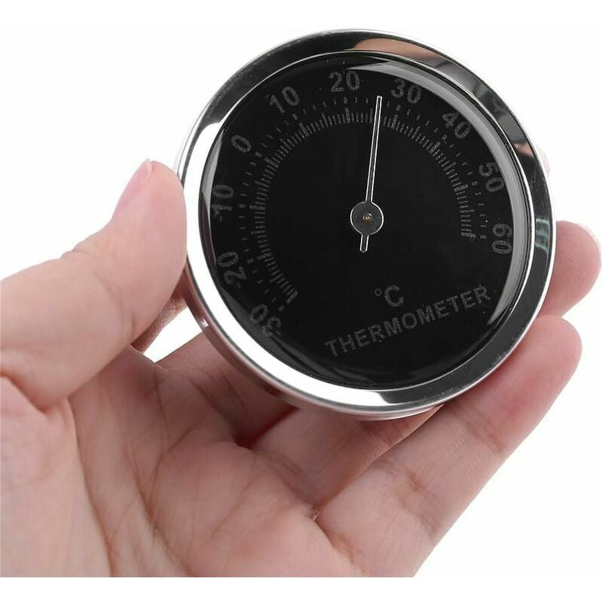 Thermometer in der Hand, zeigt ein schwarzes Zifferblatt mit Temperaturanzeigen.