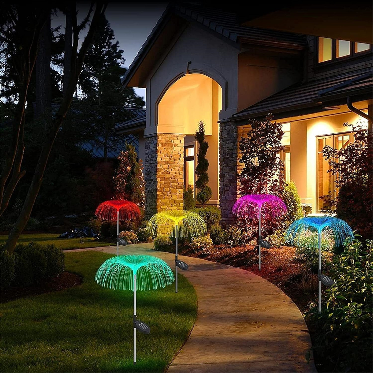 Fünf farbige Solar-Gartenleuchten auf einem Weg vor einem Haus bei Nacht.