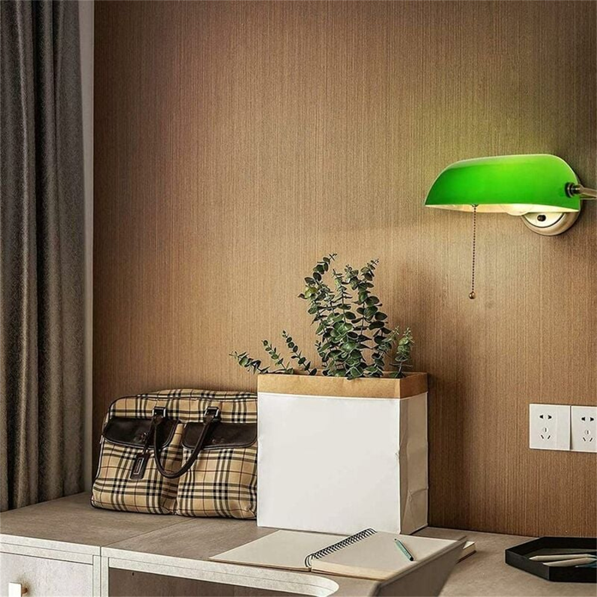 Grüne Lampe an brauner Wand, Pflanze im Topf, Tasche auf dem Schreibtisch.