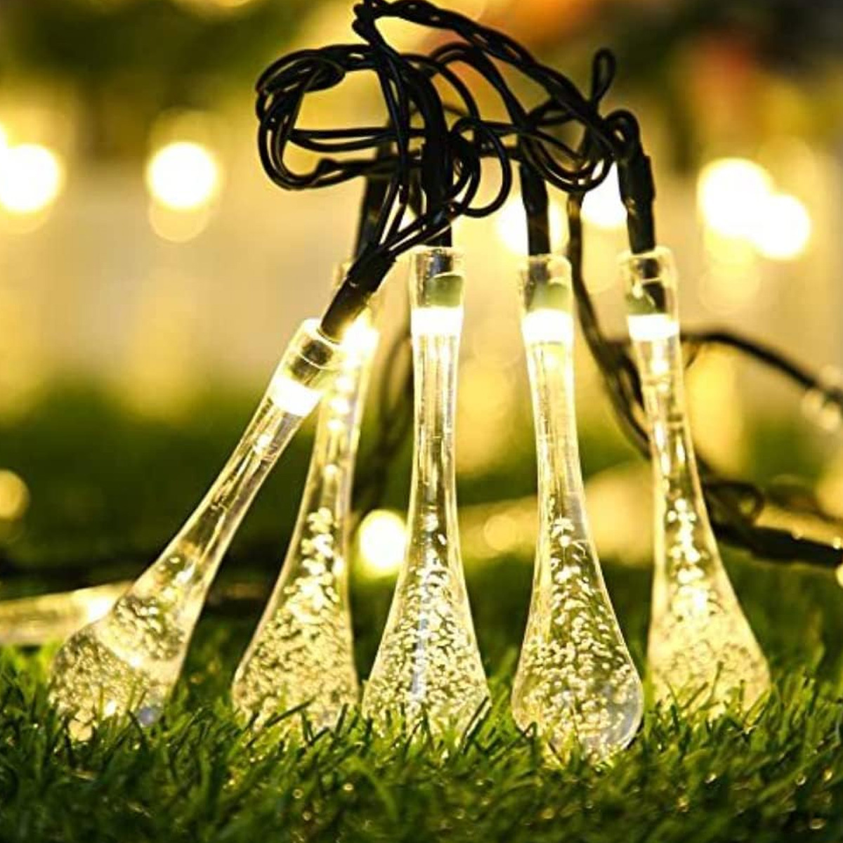 Lichterketten mit tropfenförmigen Glühbirnen liegen auf grünem Gras.