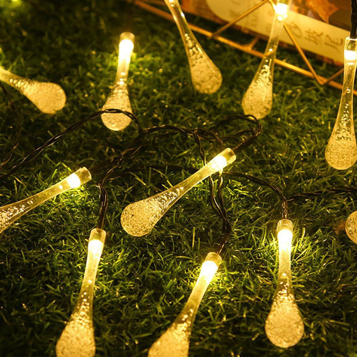 Lichterkette mit leuchtenden tropfenförmigen Glühbirnen auf grüner, grasiger Oberfläche.