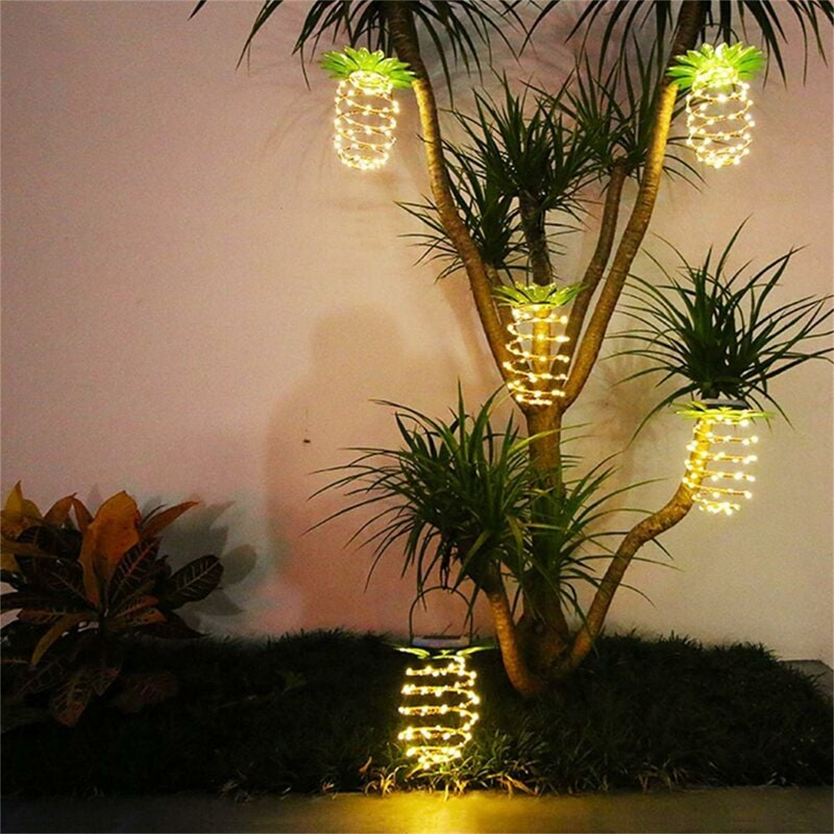 Ananasförmige Lichterketten hängen an einem Baum in einer Außenumgebung.