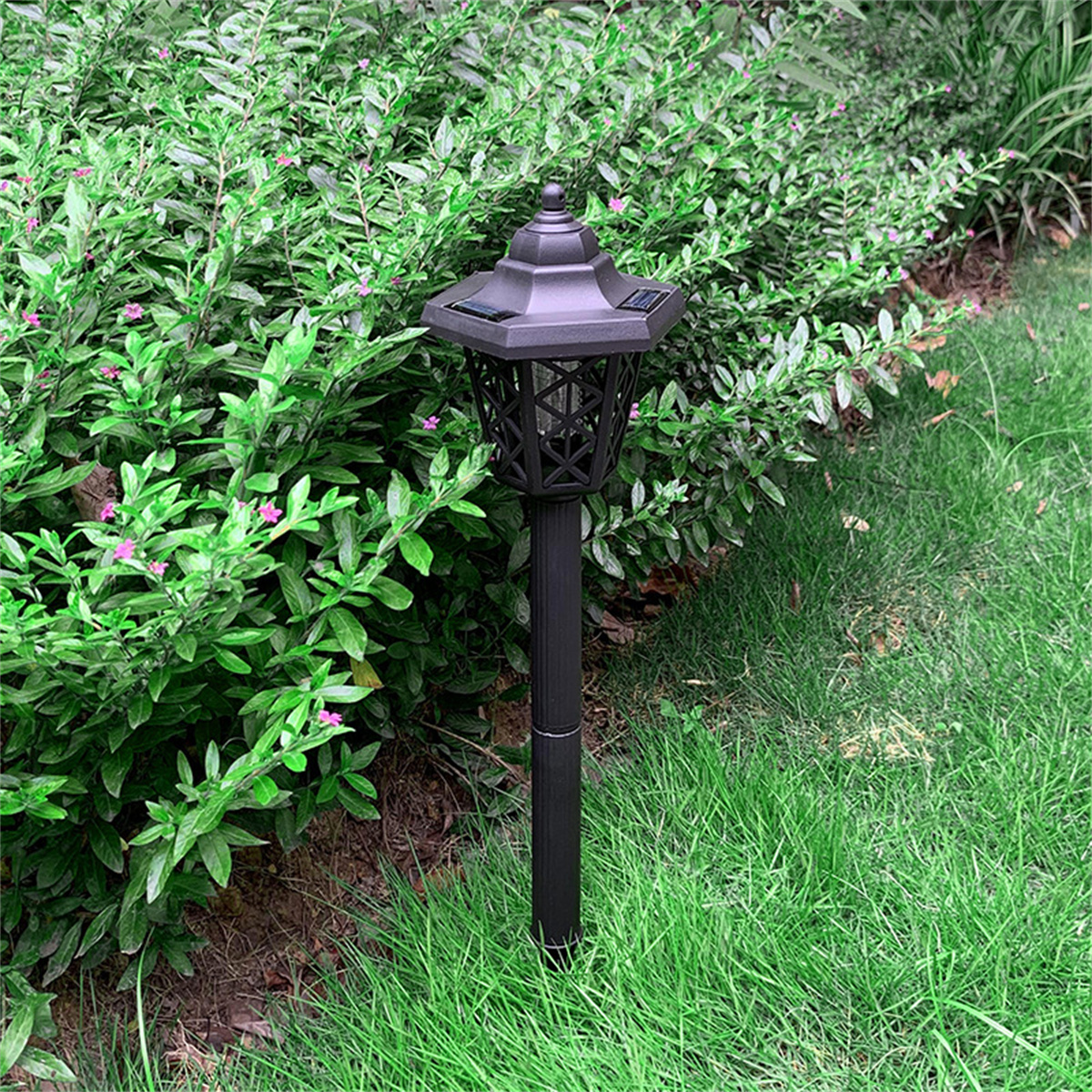 Schwarze solarbetriebene Gartenlampe in einem Garten mit grünem Gras und Büschen.