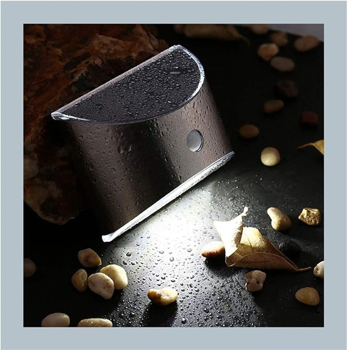 Eine kleine metallische Taschenlampe mit Wassertropfen auf dunkler Oberfläche mit kleinen Steinen.