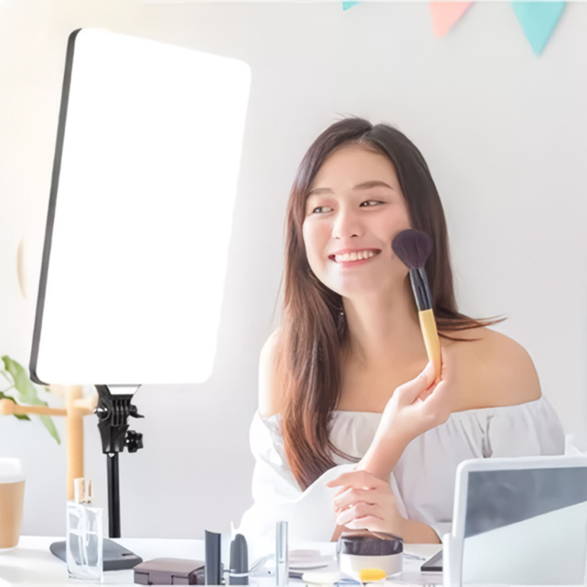 Mujer maquillándose con brocha, luz brillante, productos sobre superficie blanca.