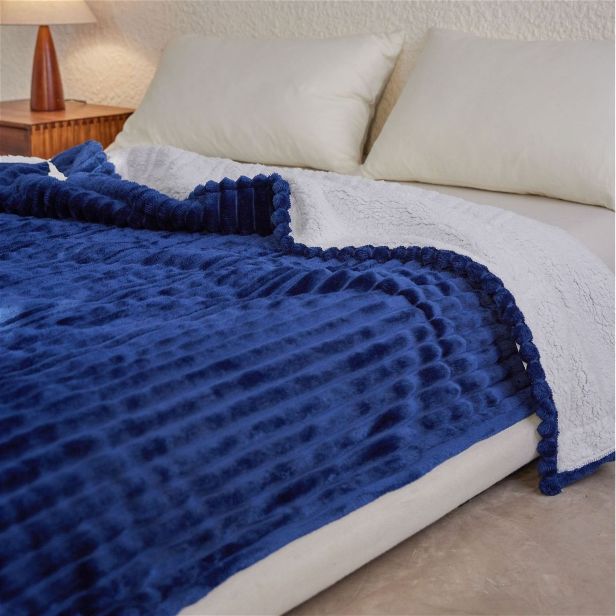 Eine blaue und weiße Wendedecke mit gerippter Textur und weißem Sherpa-Futter, die auf einem Bett liegt.