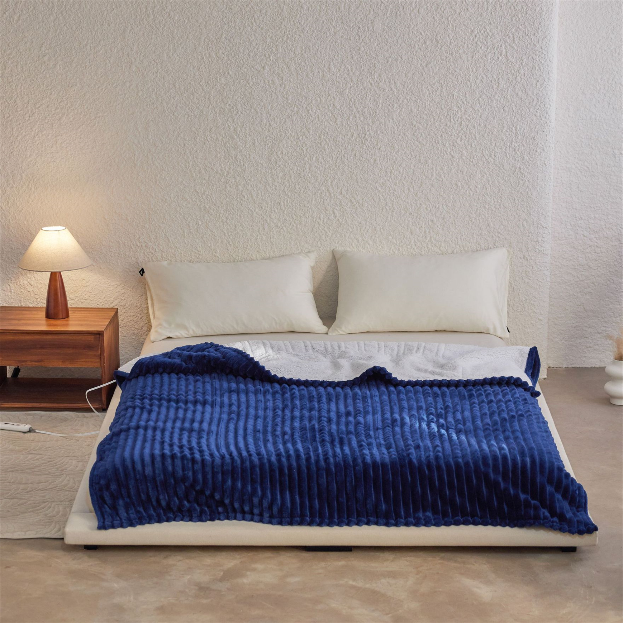 Schlafzimmer mit Bett, bedeckt mit blauer Decke, zwei Kissen, Lampe auf Nachttisch.