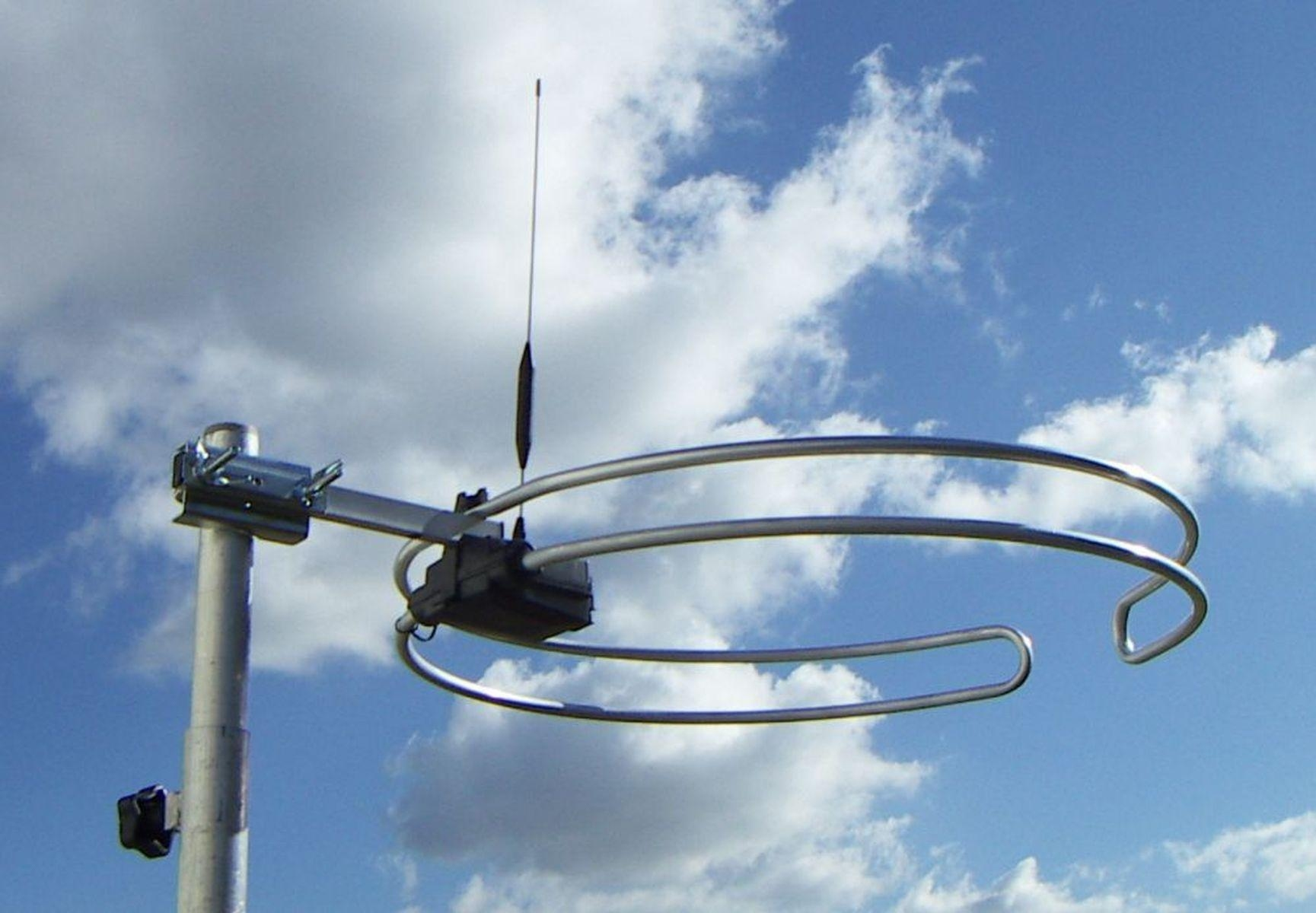 Ein Metallmast mit einer Antenne und kreisförmigen Elementen gegen blauen Himmel.