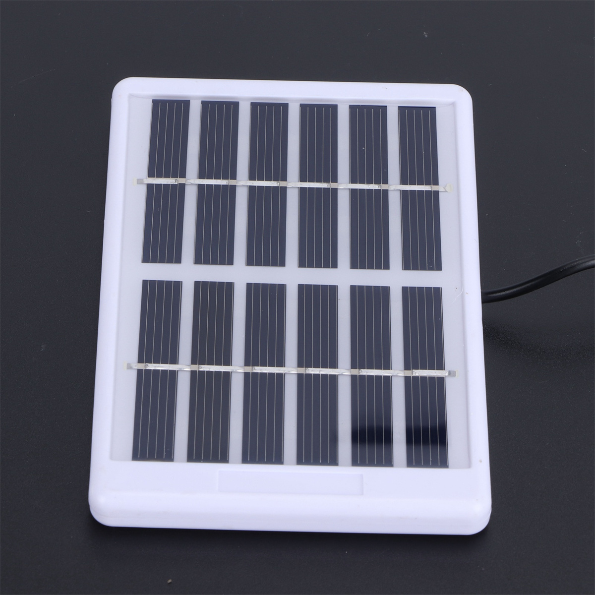 Ein kleines Solarpanel mit dunkelblauen Zellen, weißem Rahmen und schwarzem Kabel auf schwarzem Untergrund.
