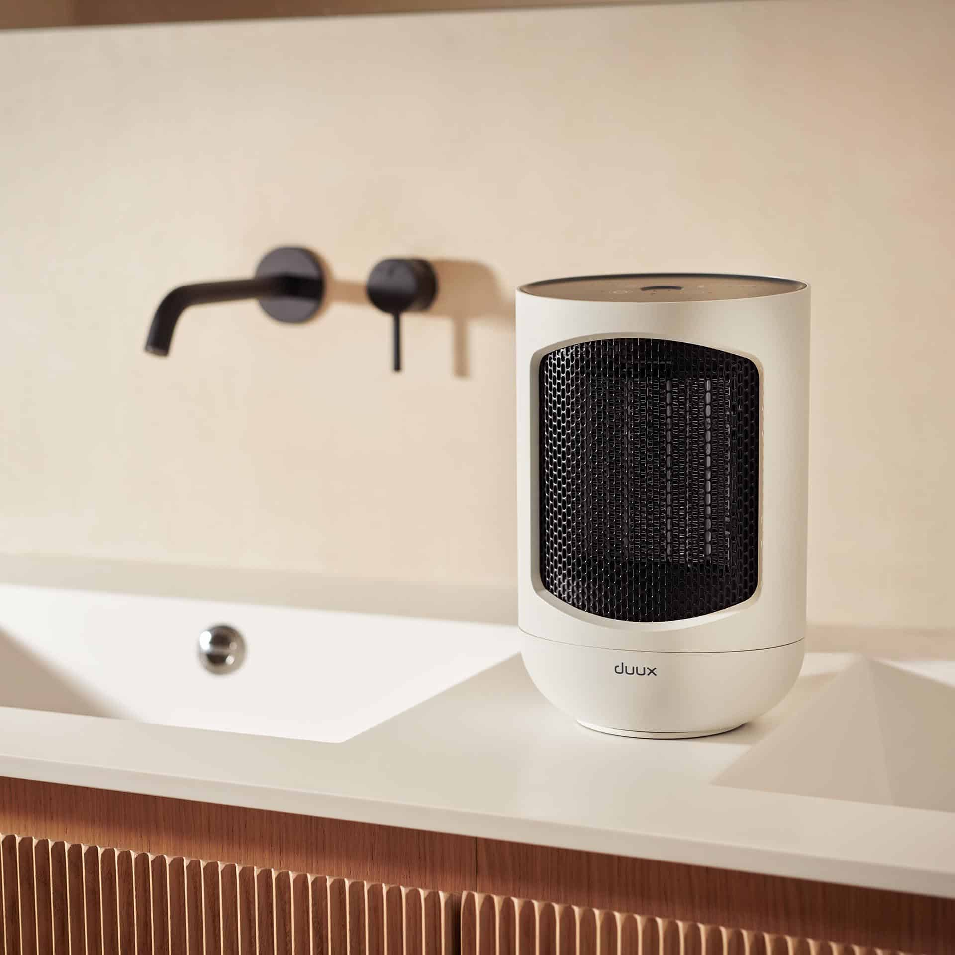 A white electric heater on a white countertop. It is in front of a sink and a wall.
