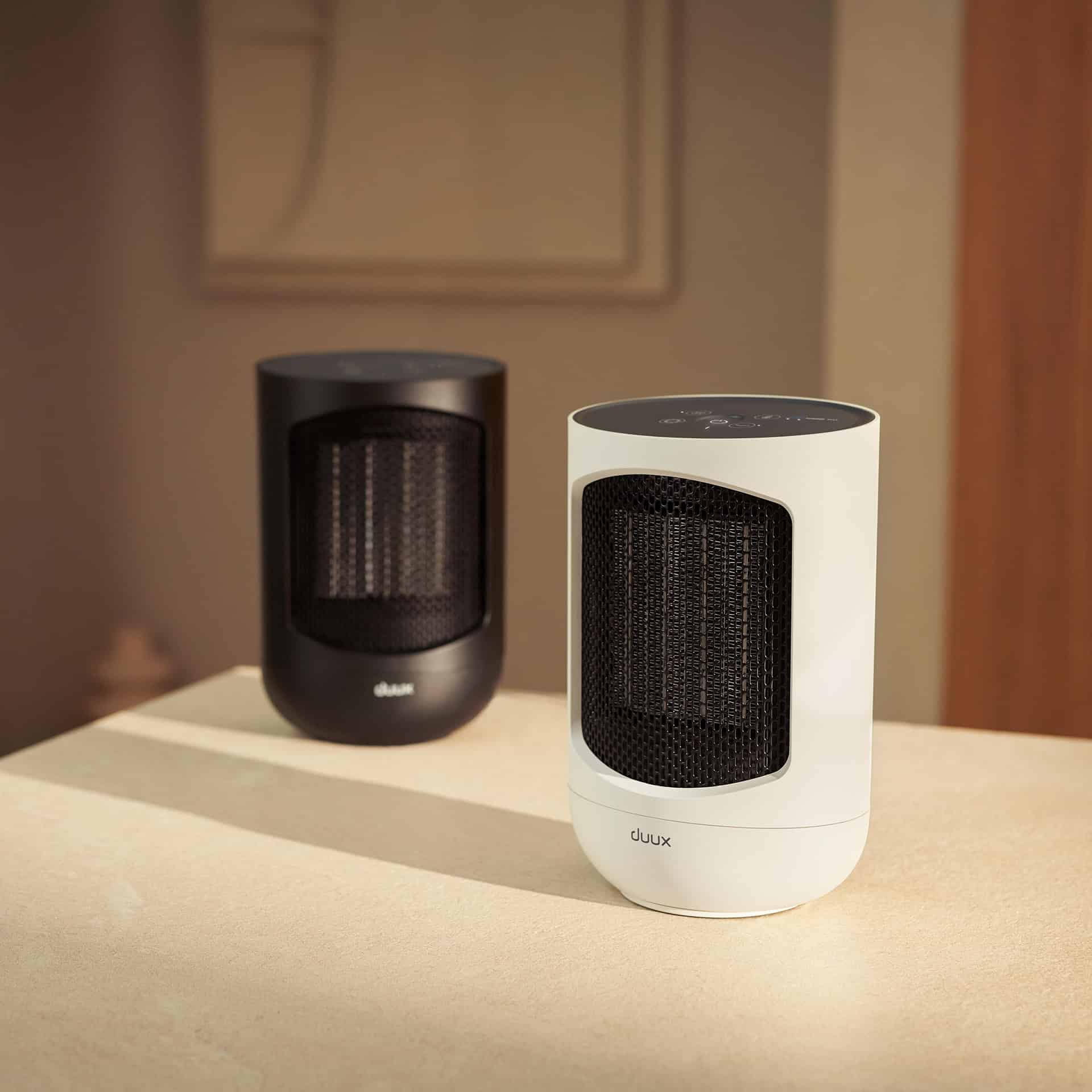 Two cylindrical heaters, one black and one white, sit on a table. A framed picture hangs in the background.