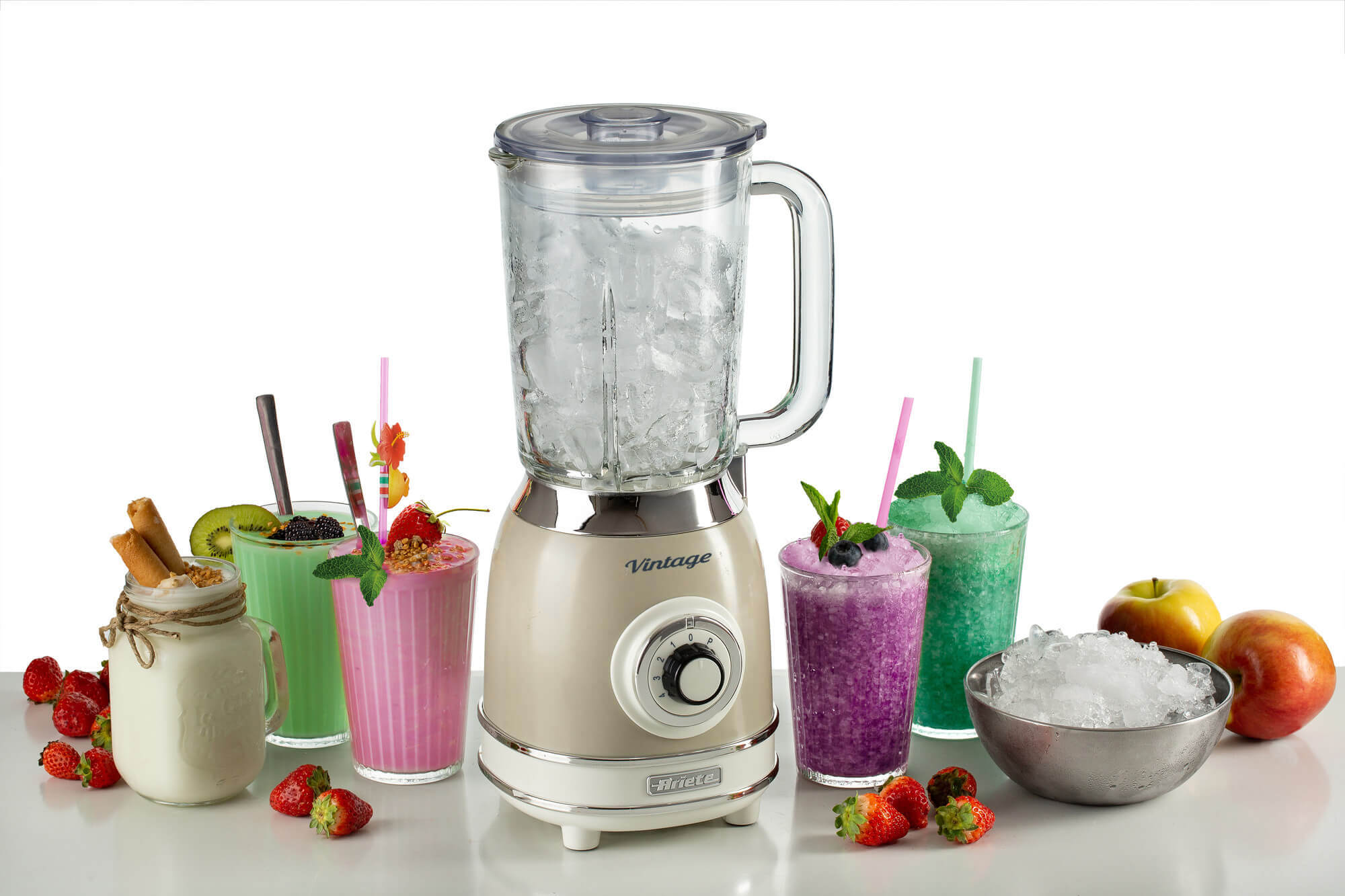 Beyaz bir yüzey üzerinde buz ve bardaklarda renkli içecekler ve meyveler bulunan bej bir blender.