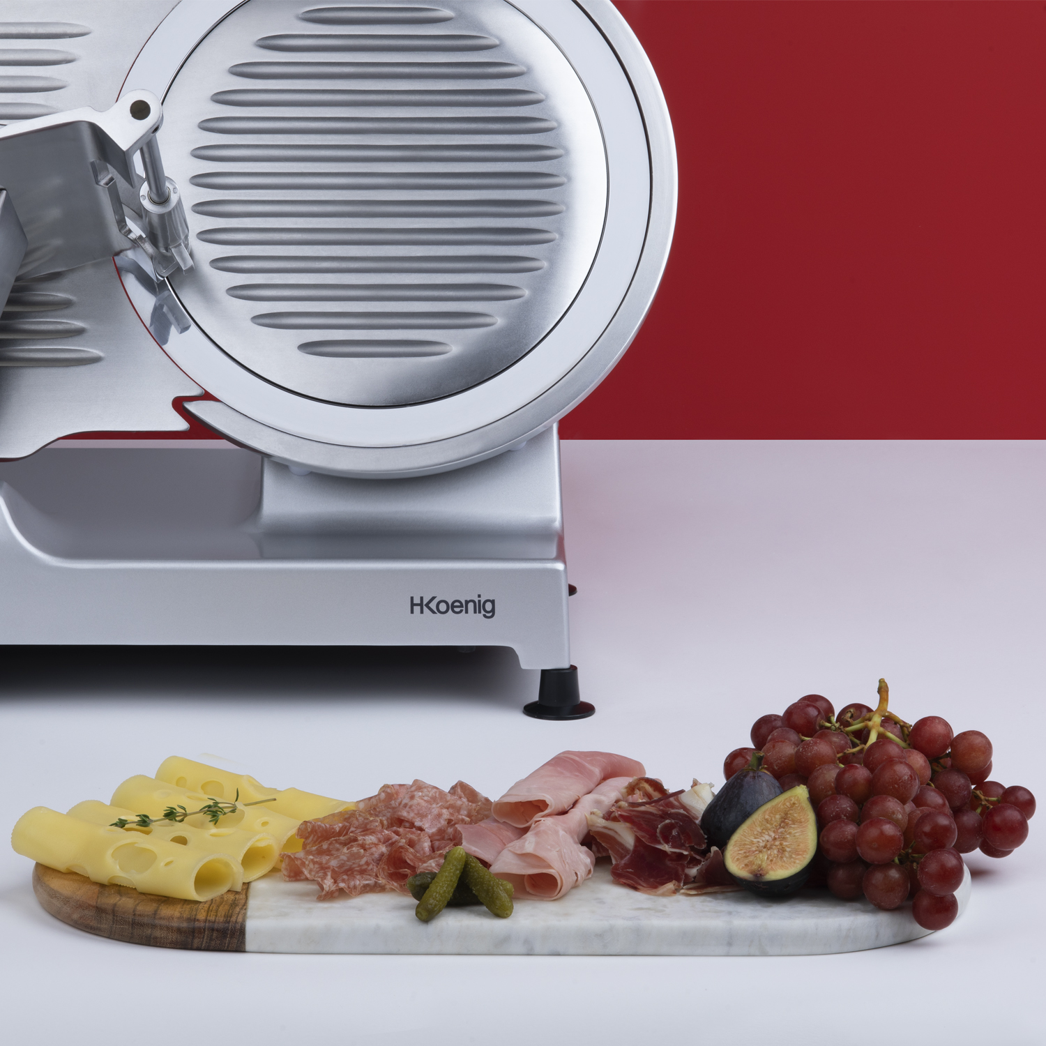 Krajalnica do żywności z serem, mięsem i winogronami na marmurowej desce.