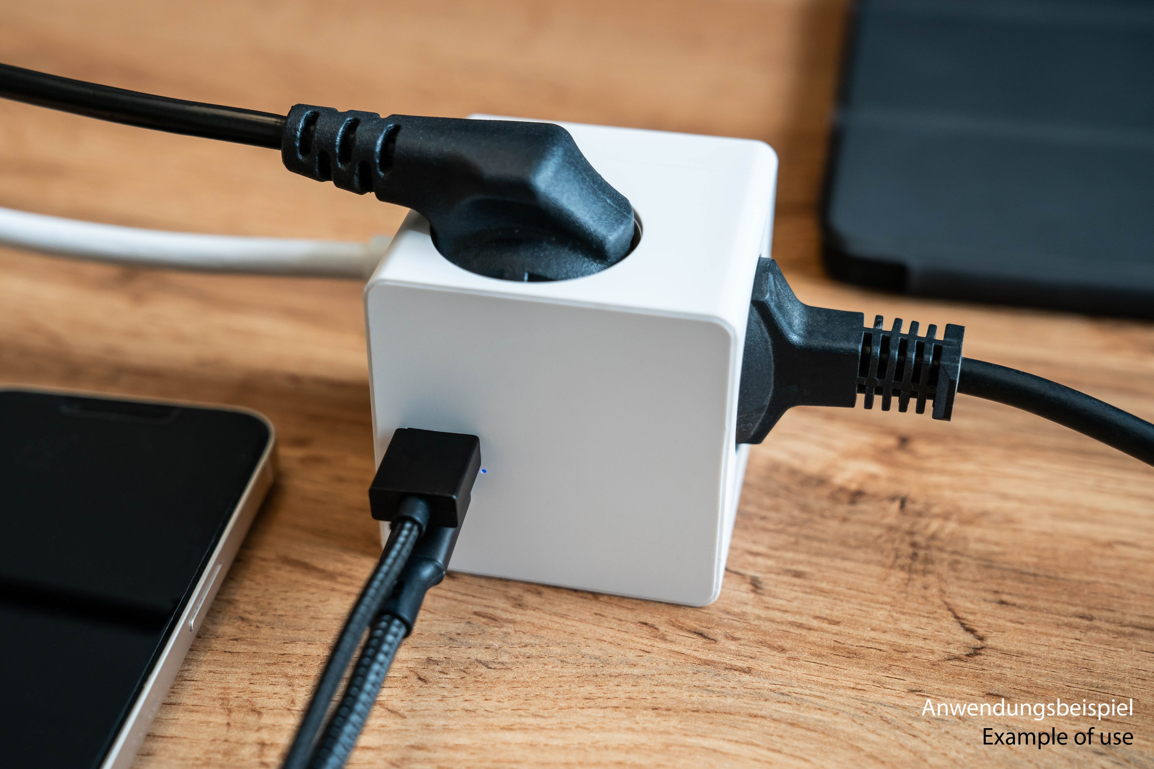 Biała kostka zasilająca z trzema wtyczkami i wpiętym kablem. Znajduje się na drewnianej powierzchni.