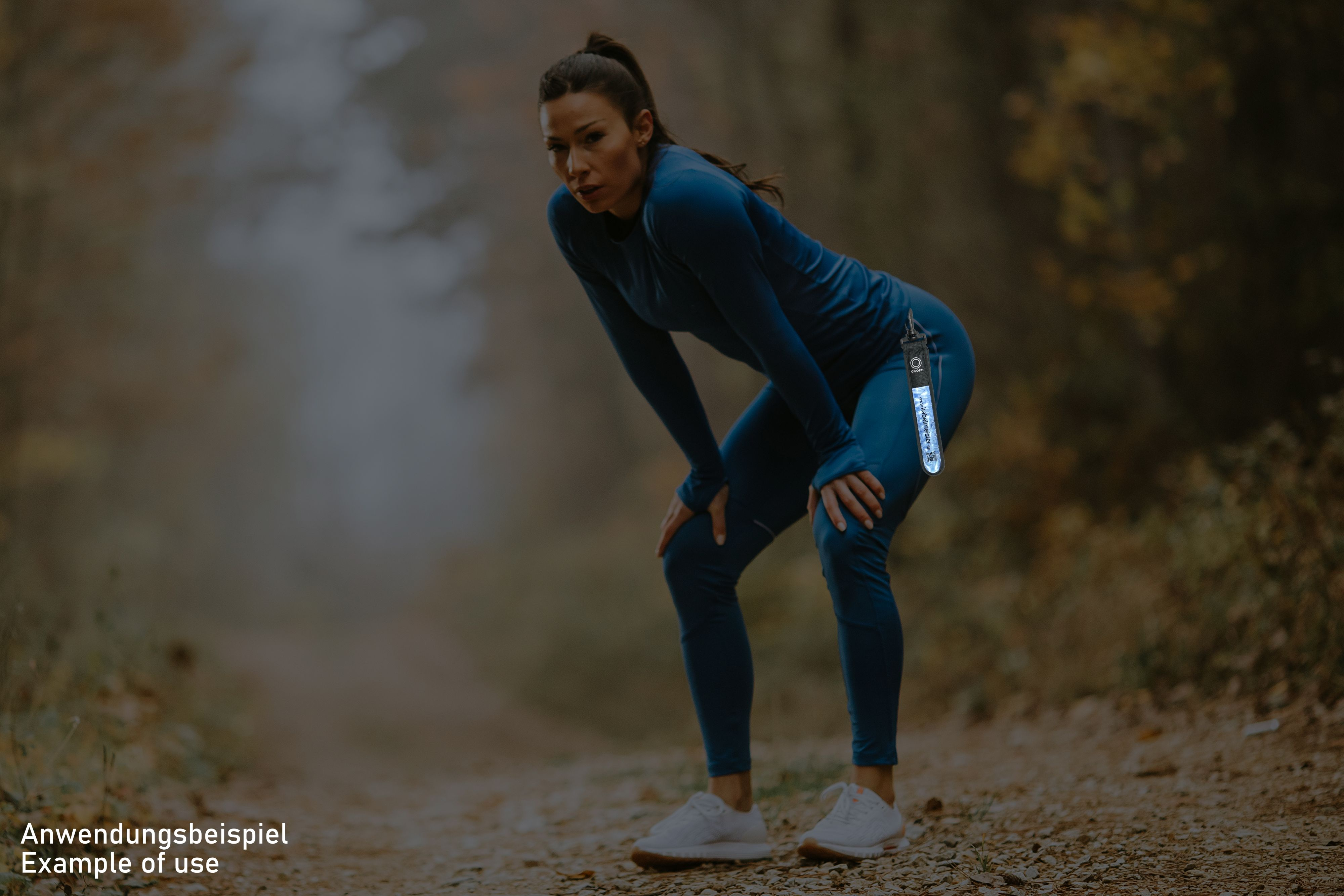 Frau in Sportkleidung. Sie macht Pause, Hände auf den Knien, im Wald. Text auf einem Schlüsselanhänger.